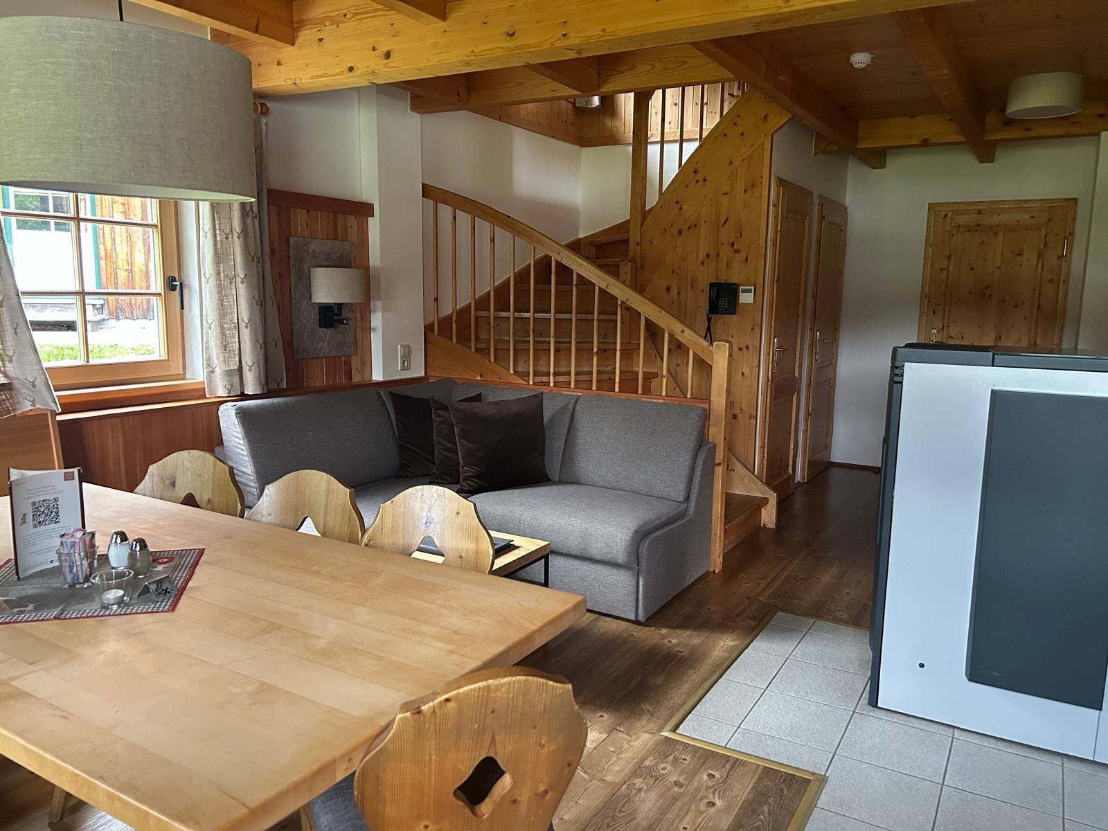 Gemütlicher Wohn-Essbereich mit Holzbalken, rustikalen Möbeln und einer Holztreppe.