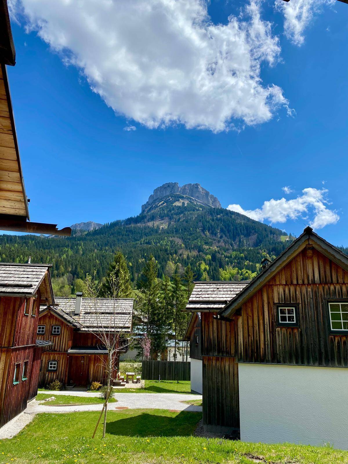 Mehrere traditionelle Holzhäuser im Chalet-Stil mit beeindruckendem Bergblick unter blauem Himmel.