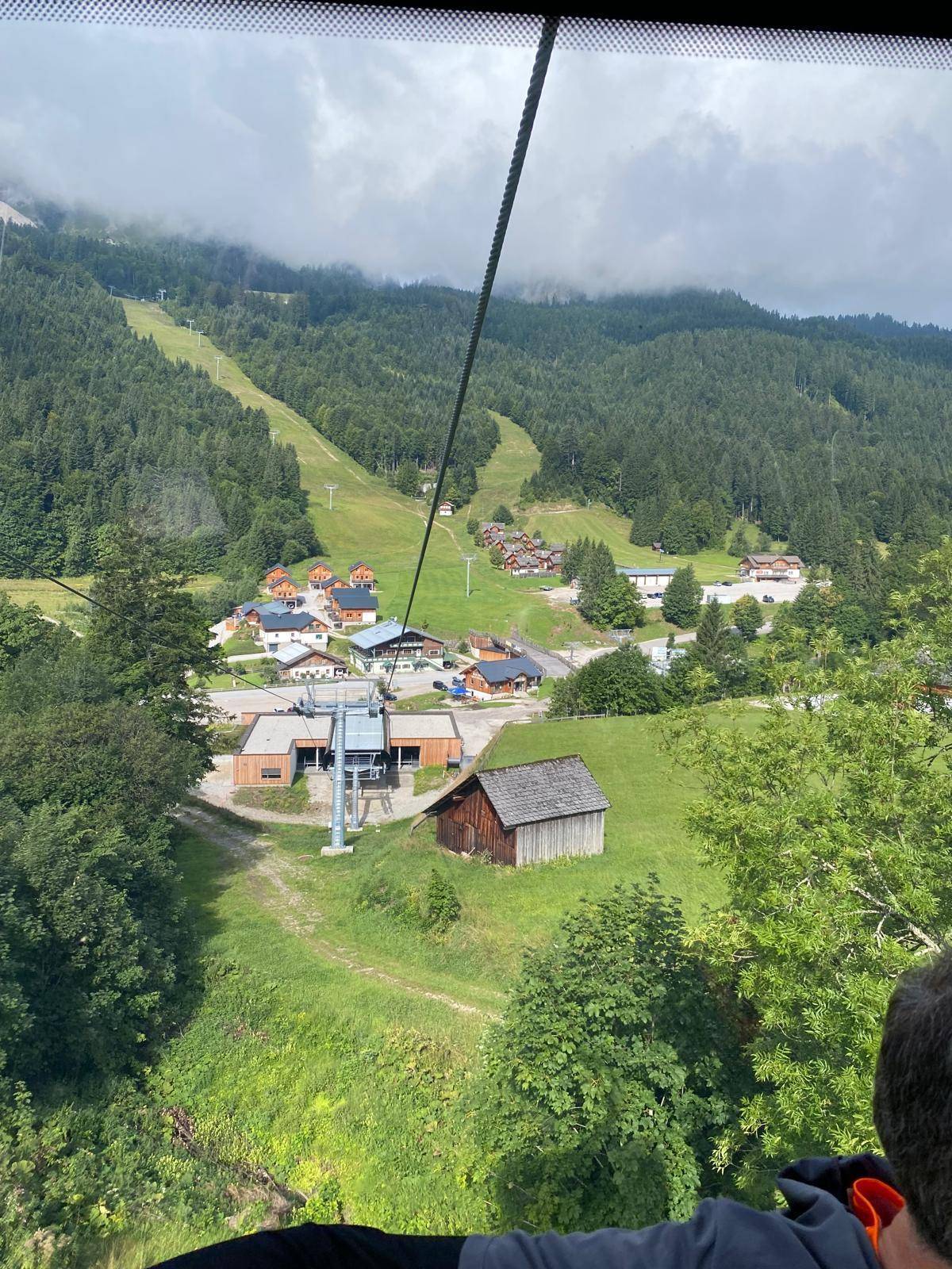 Luftaufnahme eines Skigebiets mit Chalets, Skipisten und einer Seilbahnstation in den Bergen.