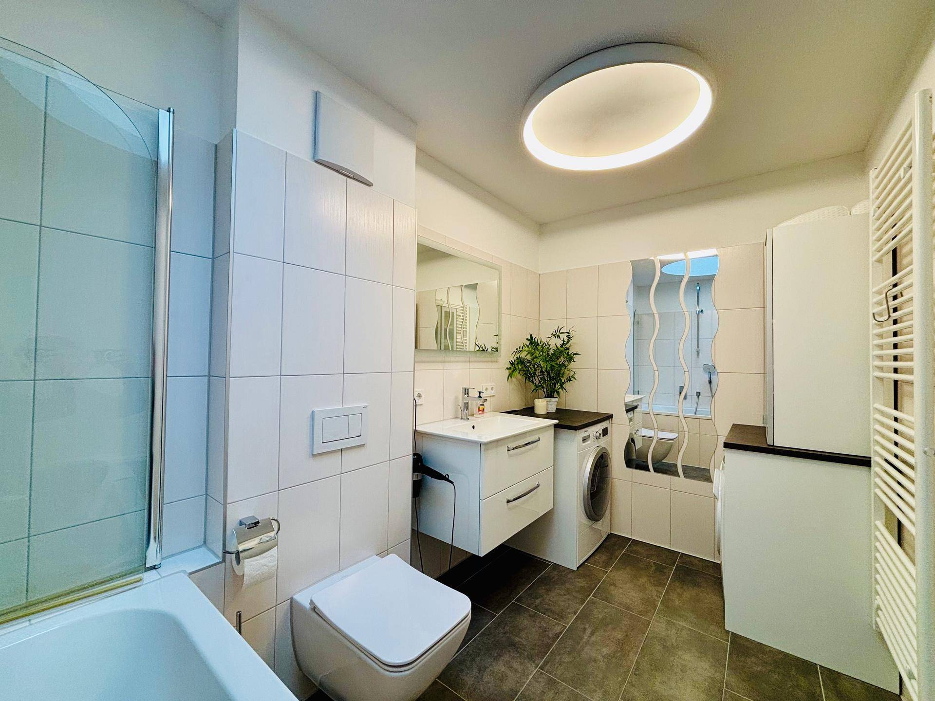 Modernes Badezimmer mit Badewanne, Dusche, Waschbecken und Waschmaschine.