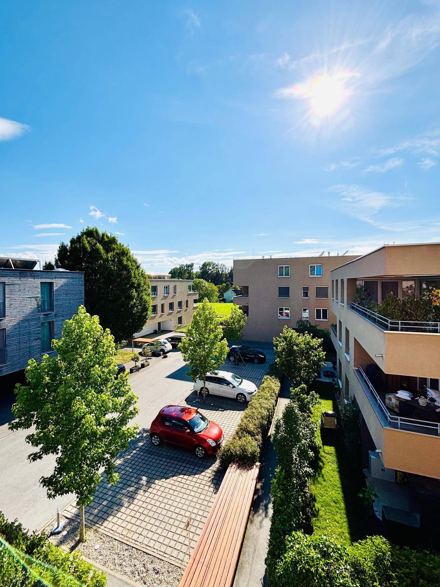 Außenansicht der Wohnanlage mit Parkplätzen, viel Grün und sonnigem Wetter.