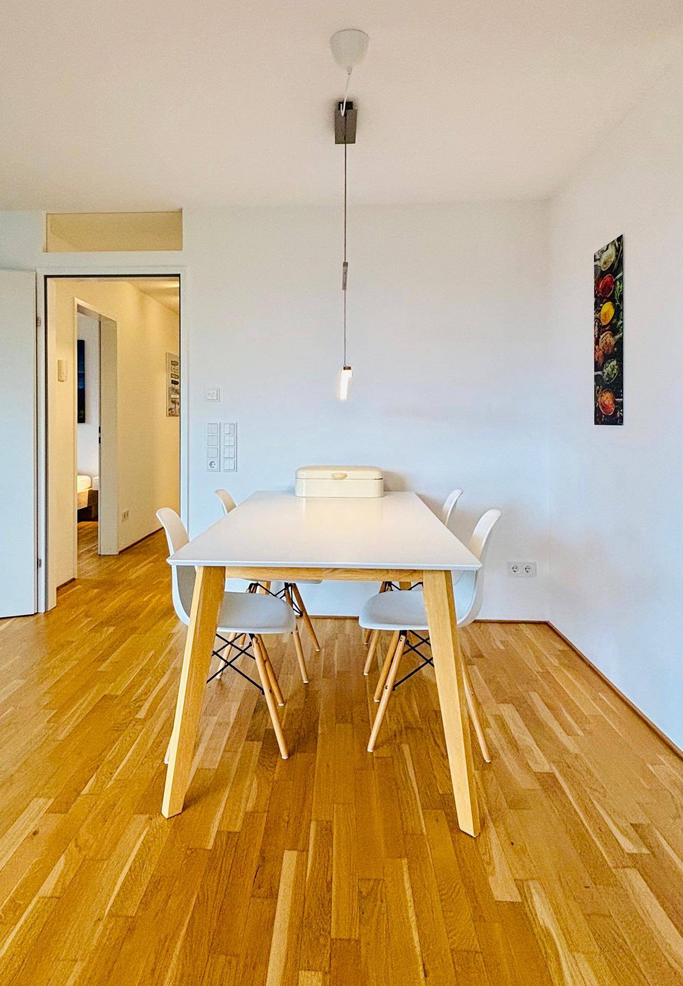 Heller Essbereich mit modernem Holztisch und weißen Stühlen, angrenzend an einen Flur.