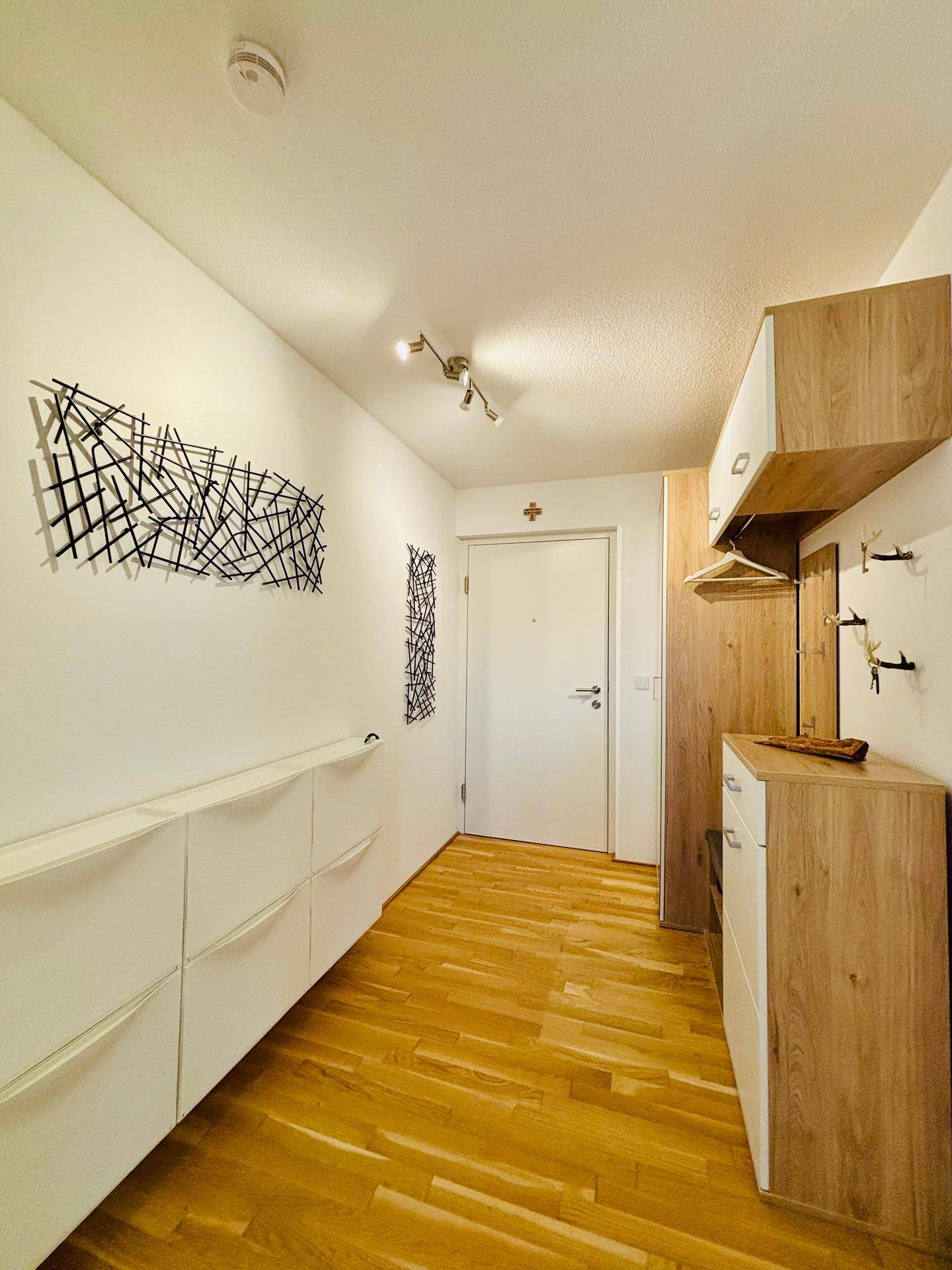 Heller Flur mit Holzboden, modernen Schuhschränken und Garderobe am Eingang.