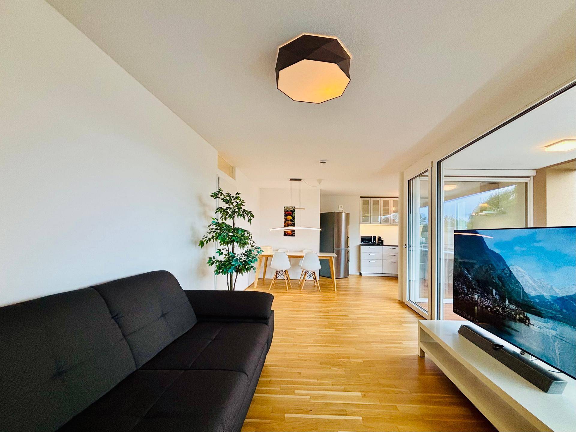 Offener Wohn- und Essbereich mit Holzboden, Sofa und Blick in die Küche.