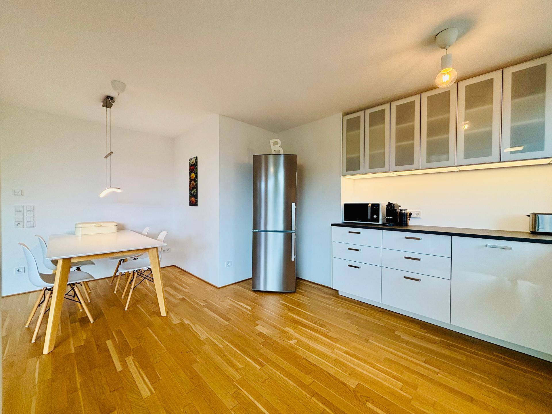 Heller Essbereich in der Küche mit modernem Tisch, Stühlen und großem Kühlschrank.