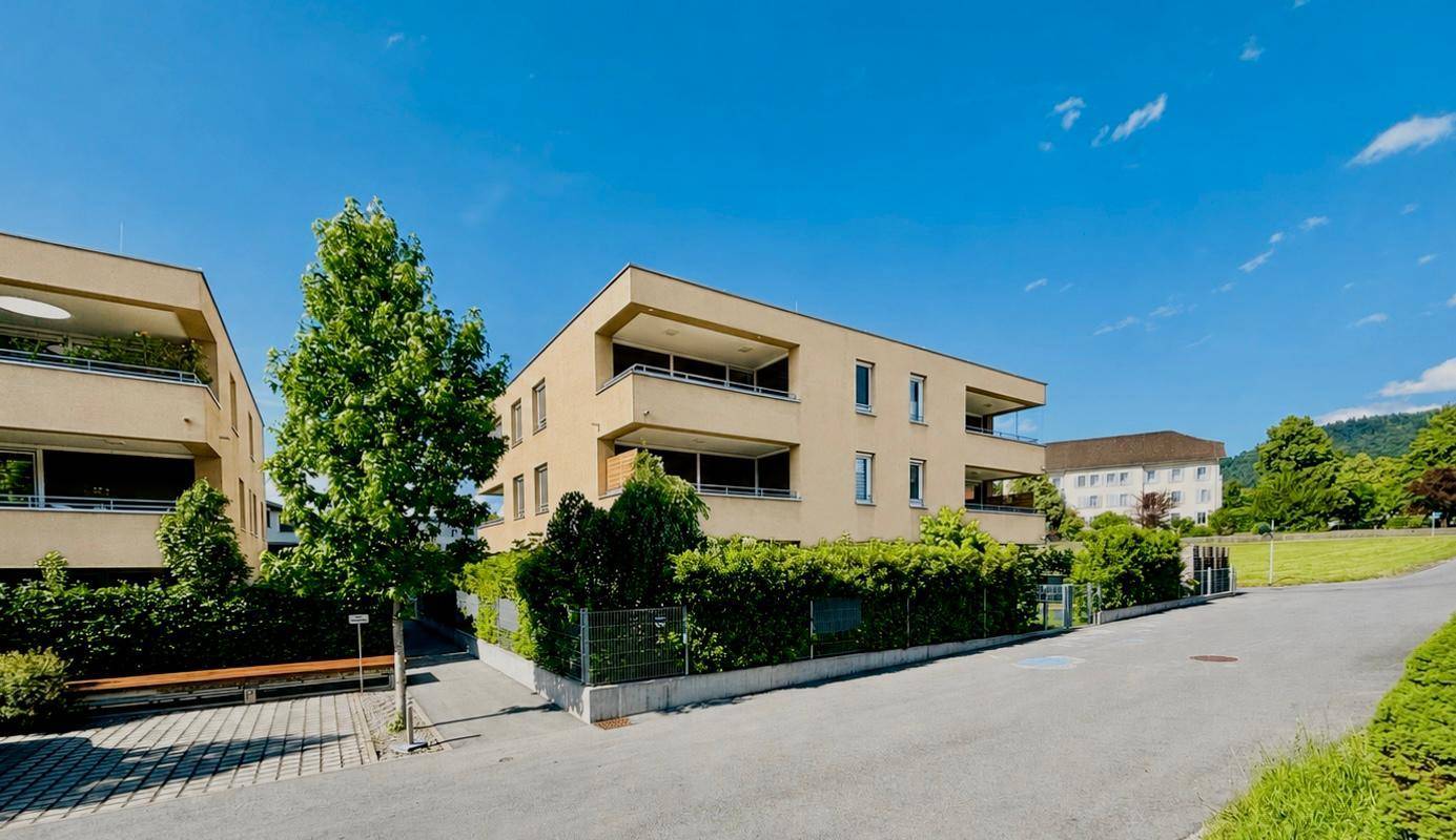 Moderne Wohngebäude in einer grünen Umgebung mit gepflegten Hecken und Bäumen.