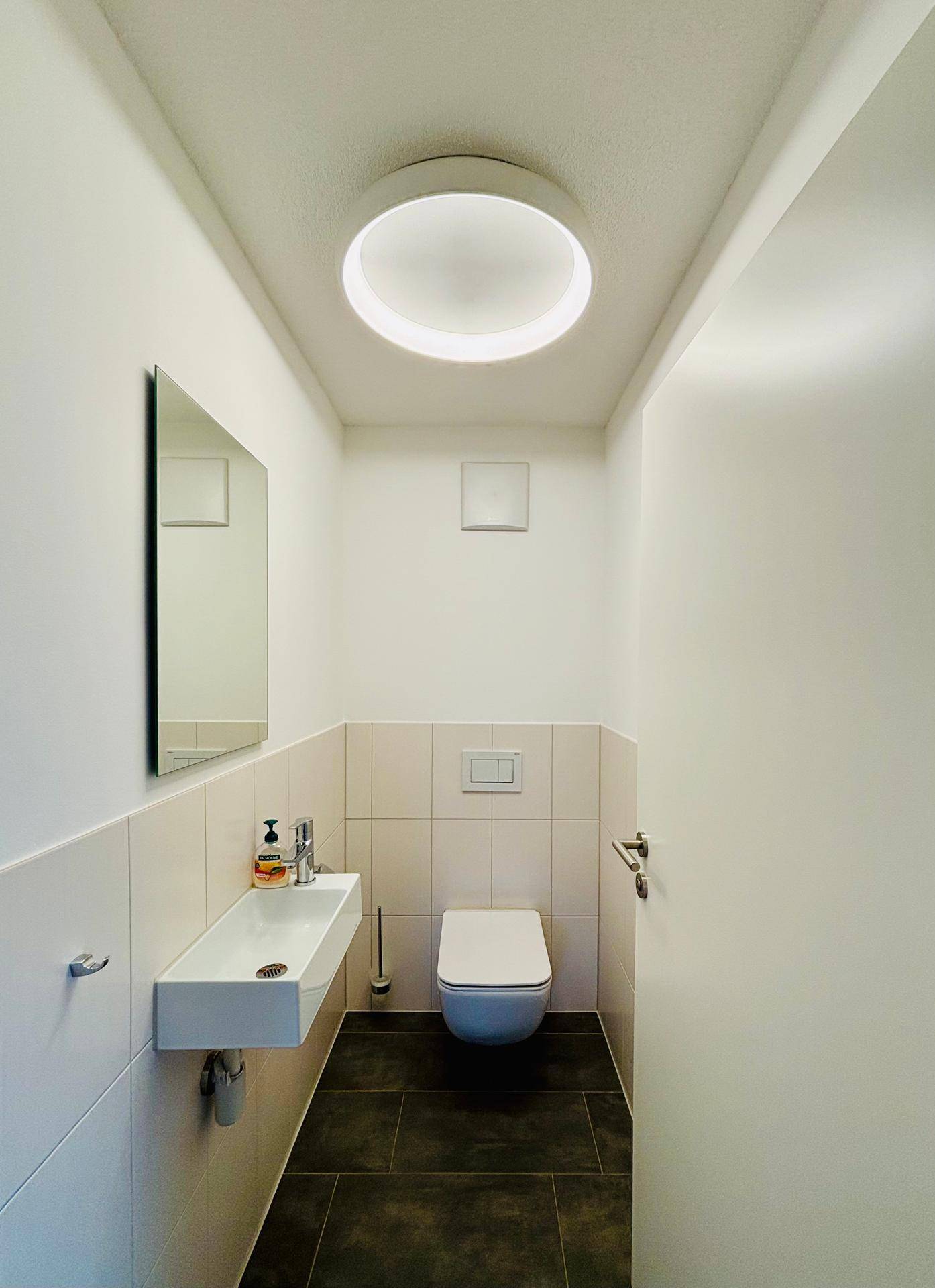 Modernes Gäste-WC mit Waschbecken, wandhängender Toilette und dunklen Bodenfliesen.