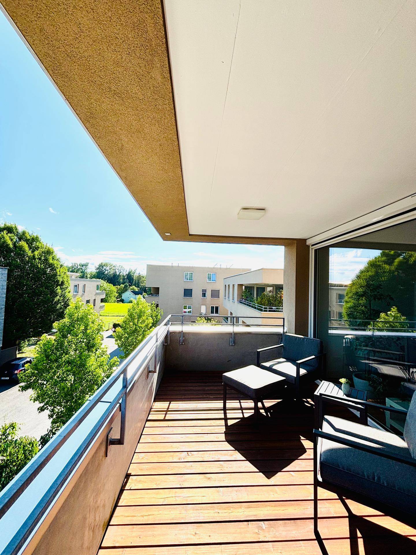 Geräumiger Balkon mit Holzbelag, Sitzgelegenheiten und Blick auf die Umgebung.