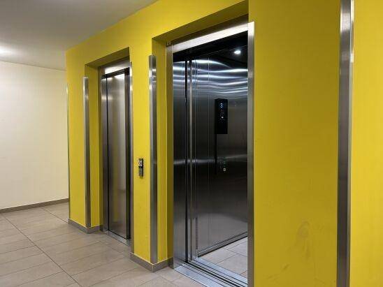 Zwei moderne Aufzüge in einem hellen Flur mit auffälliger gelber Wandgestaltung.