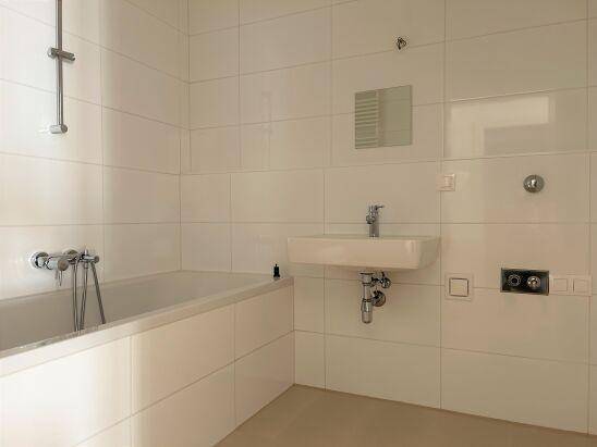 Modernes Badezimmer mit weißen Fliesen, Badewanne und wandmontiertem Waschbecken.