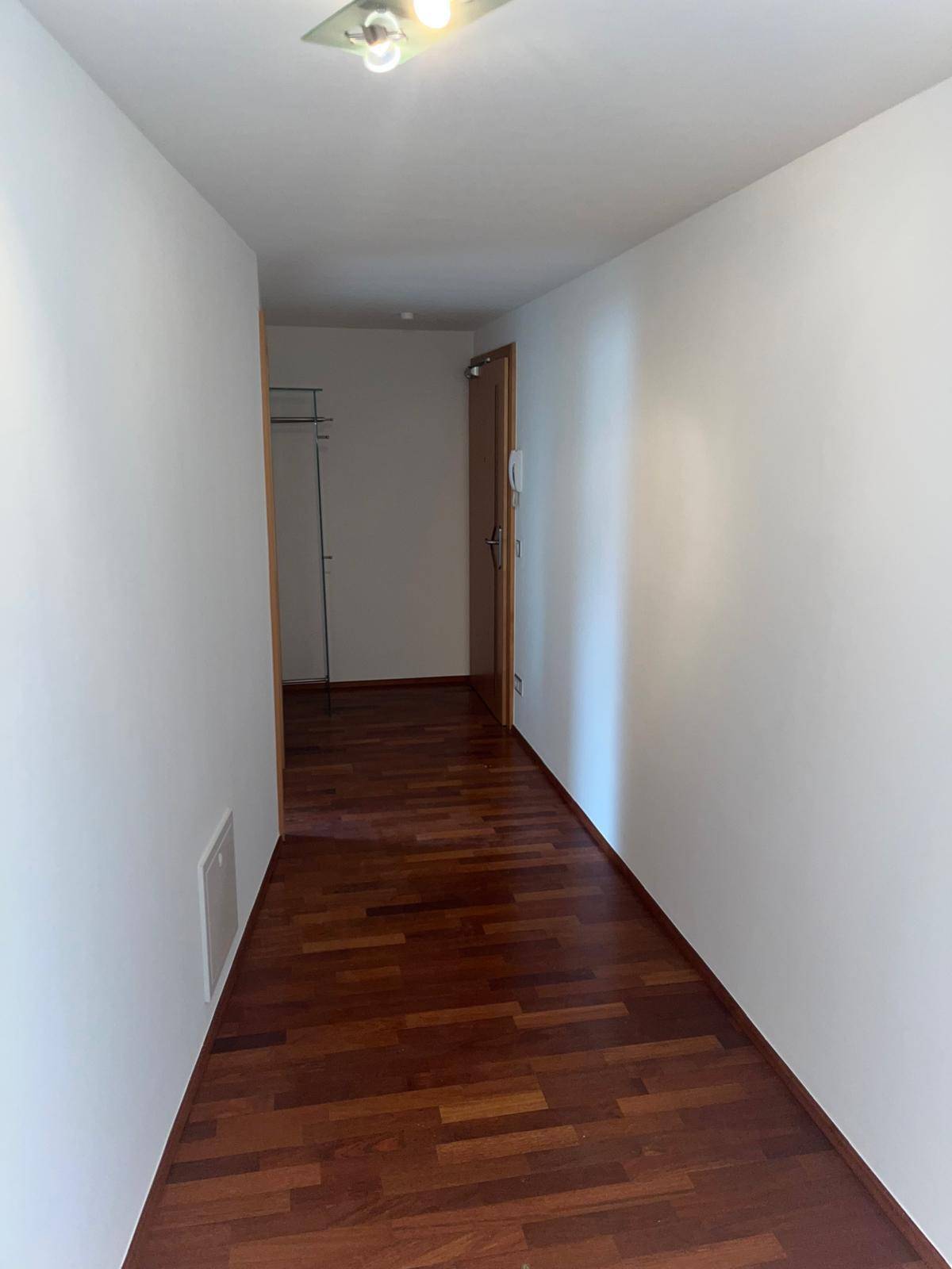 Langer, heller Flur mit dunklem Holzboden und weißen Wänden, der zu weiteren Räumen führt.