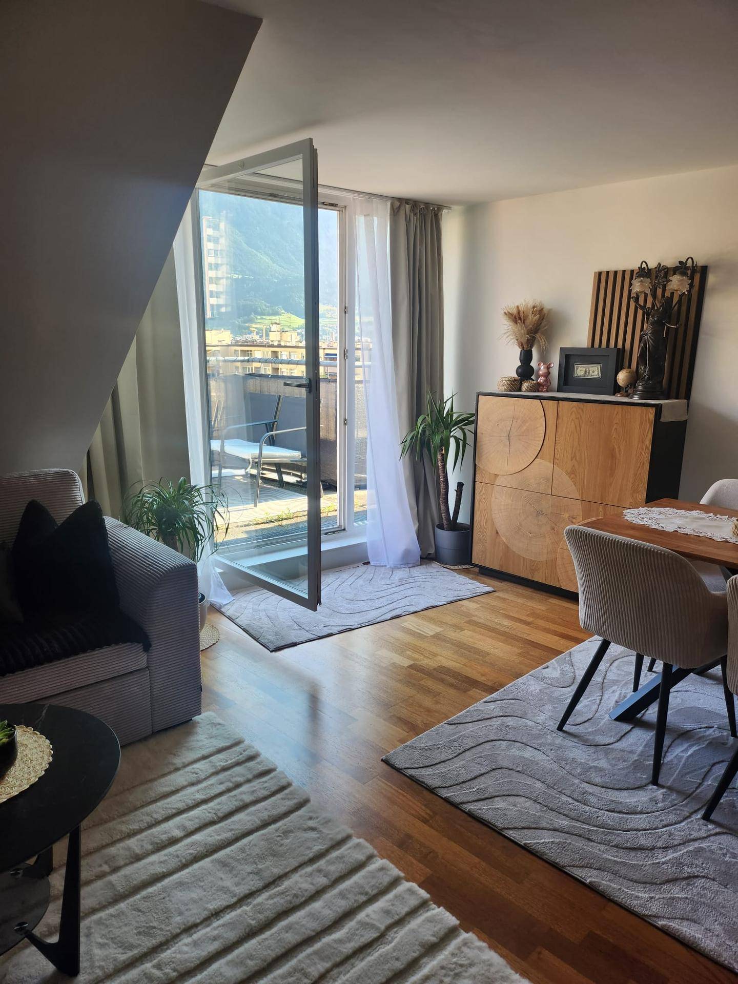 Gemütlicher Wohn-Essbereich mit Holzboden, modernen Möbeln und direktem Zugang zum Balkon.