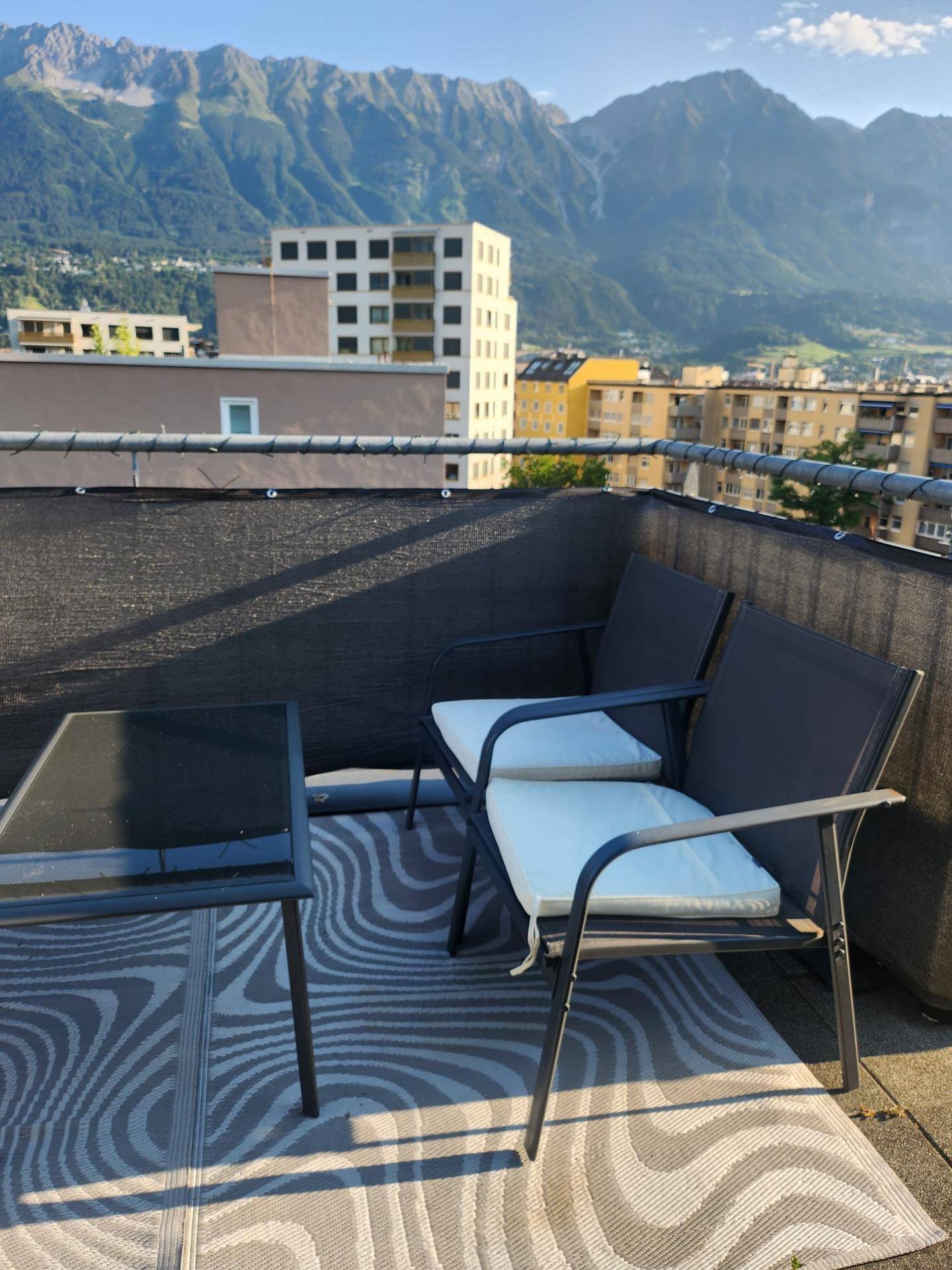Möblierter Balkon mit atemberaubendem Bergblick und Stadtpanorama unter strahlend blauem Himmel.