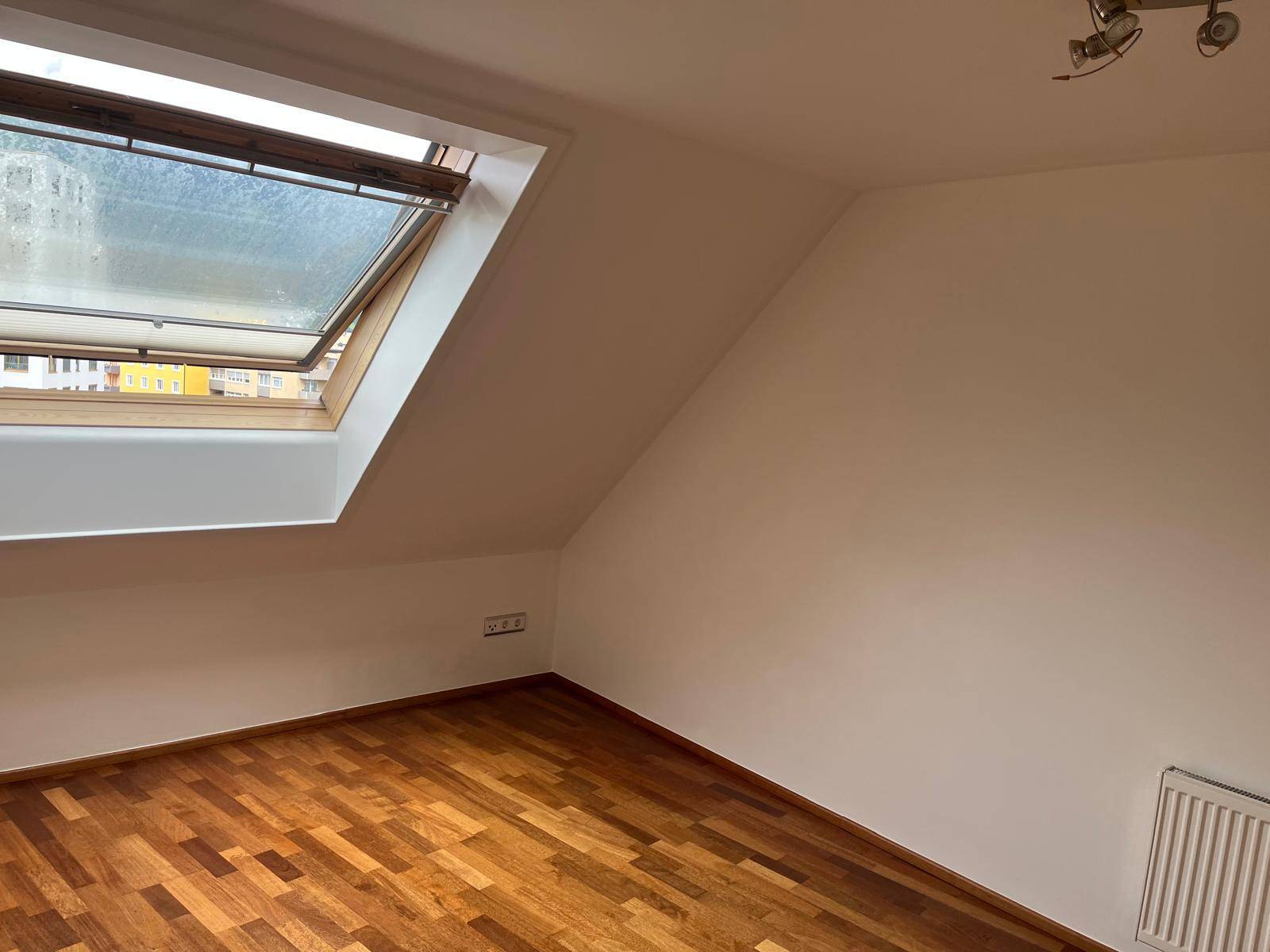 Heller Raum im Dachgeschoss mit Holzboden und einem großen Dachfenster für natürliches Licht.