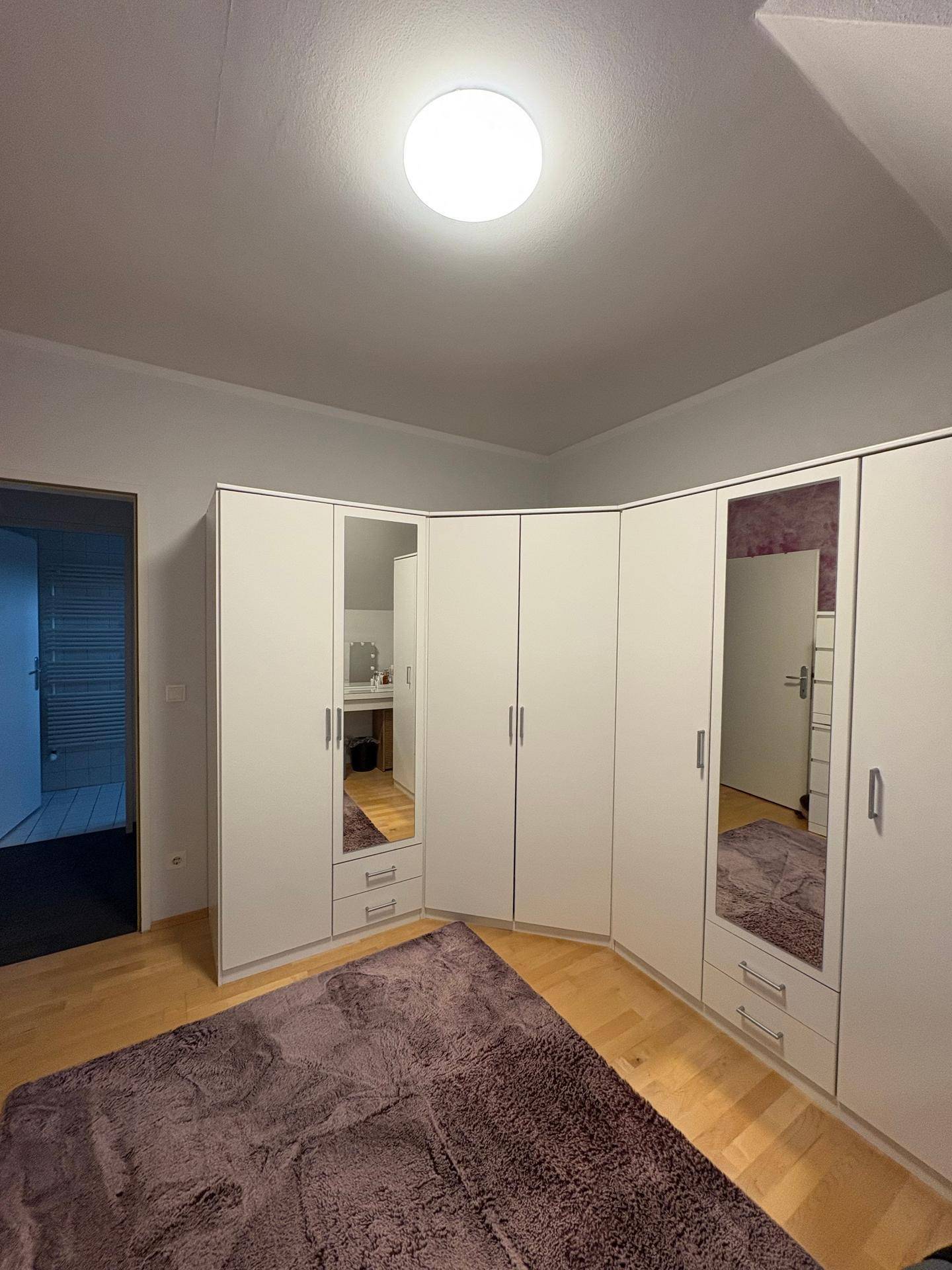 Schlafzimmer mit großem Eckkleiderschrank, Spiegeltüren und hellem Holzboden.