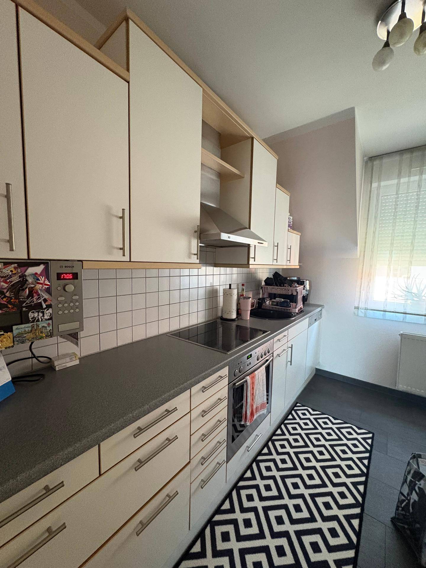 Funktionale Küche mit weißen Schränken, dunkler Arbeitsplatte, integriertem Backofen und Induktionskochfeld.