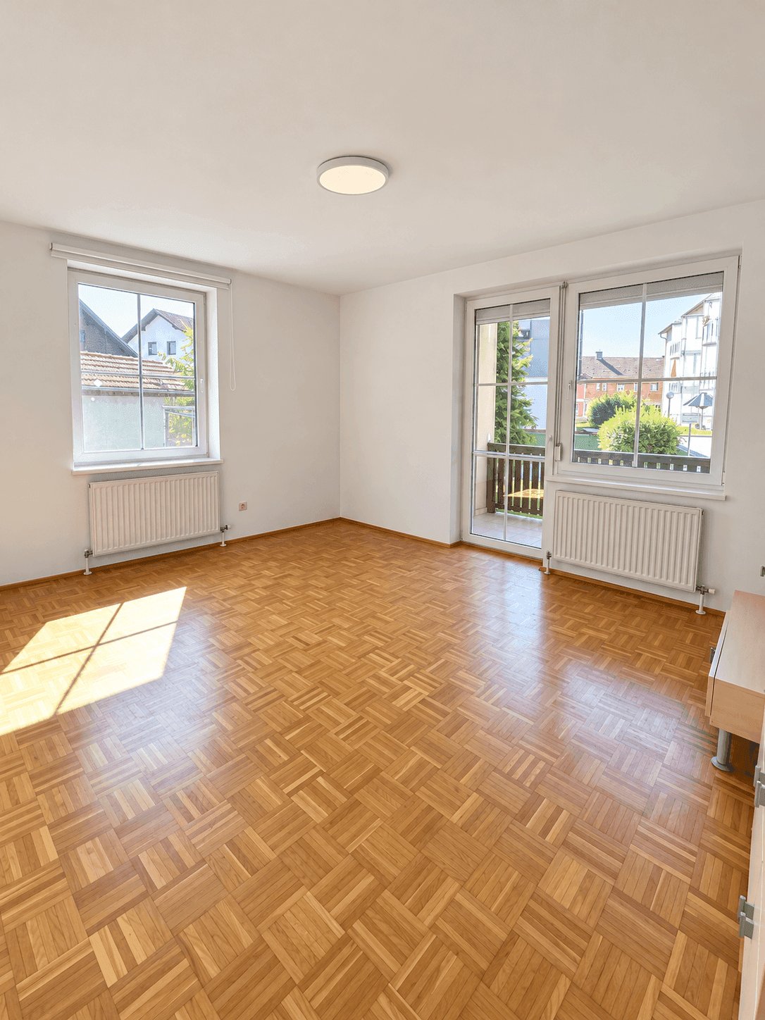 Lichtdurchfluteter Raum mit Parkettboden und Zugang zu einem französischen Balkon.