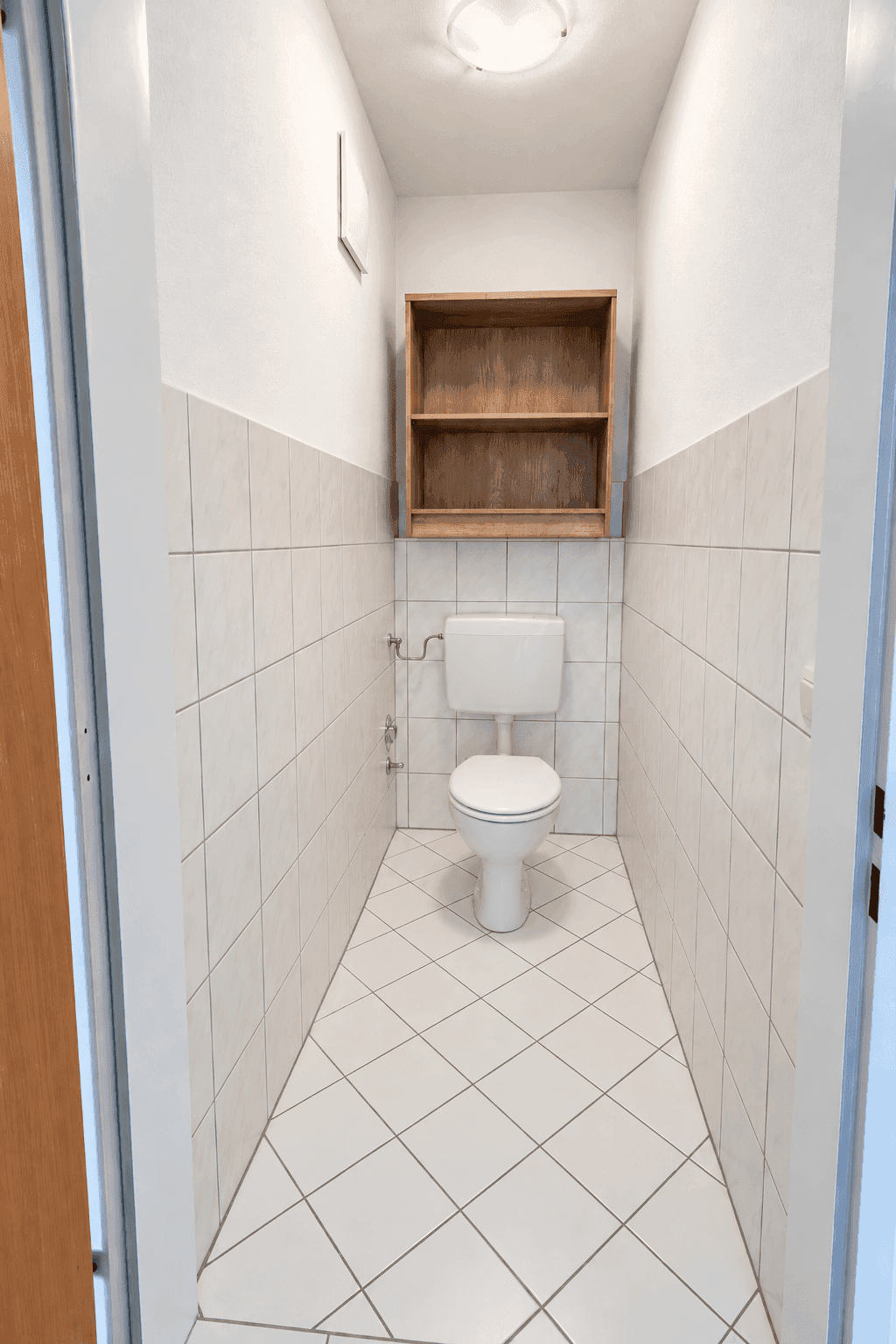 Kleines Gäste-WC mit weißen Fliesen und einfacher Toilette.