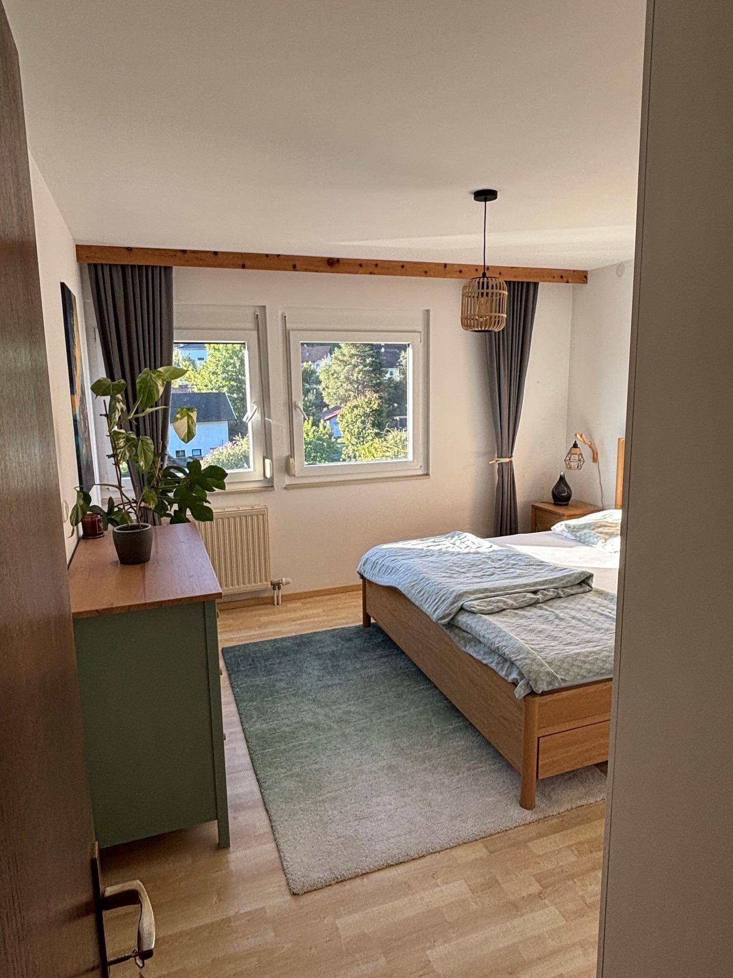 Helles Schlafzimmer mit Holzbett, Kommode und Blick ins Grüne.