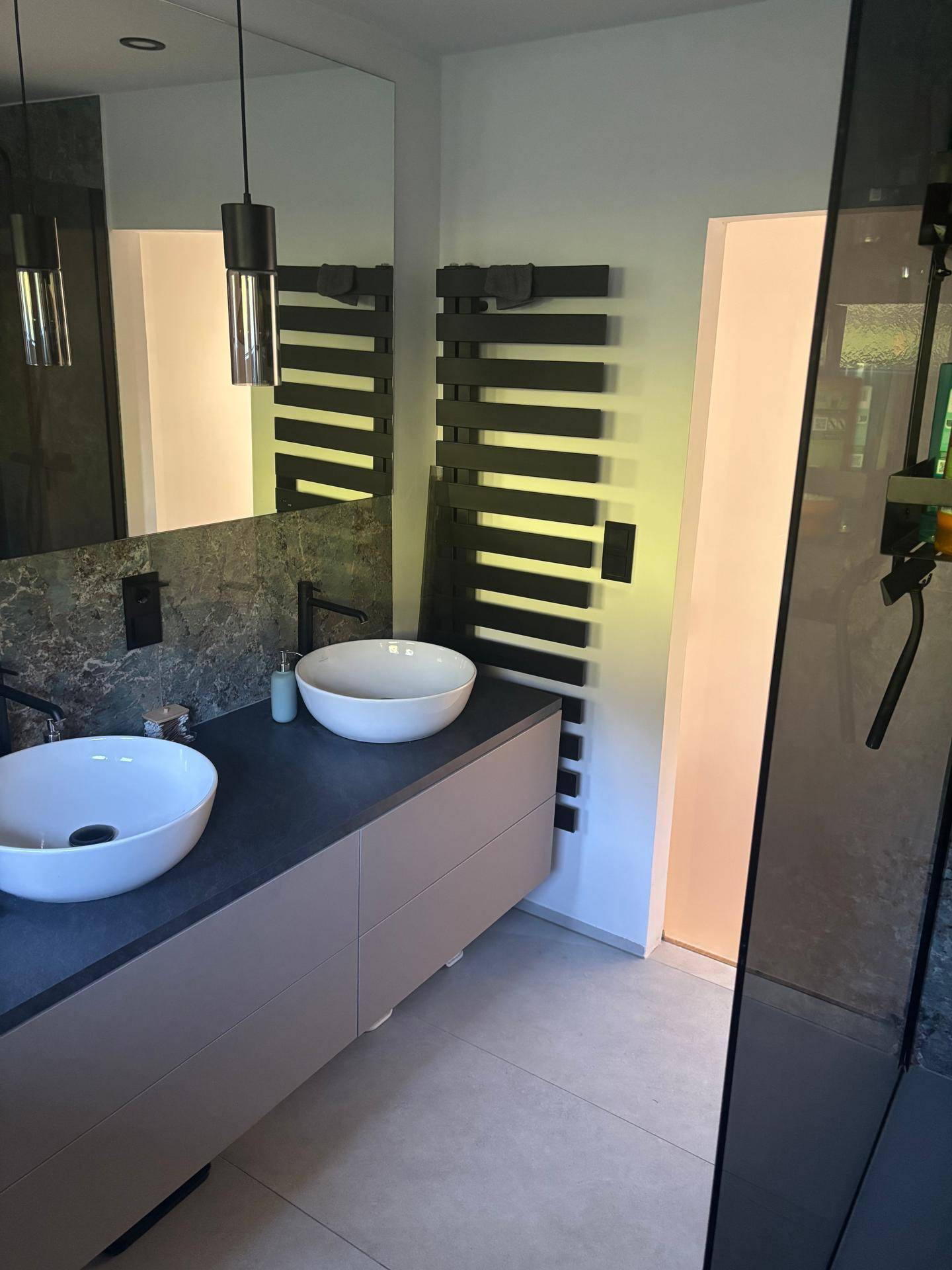 Modernes Badezimmer mit Doppelwaschbecken, dunklen Armaturen und beheiztem Handtuchhalter.