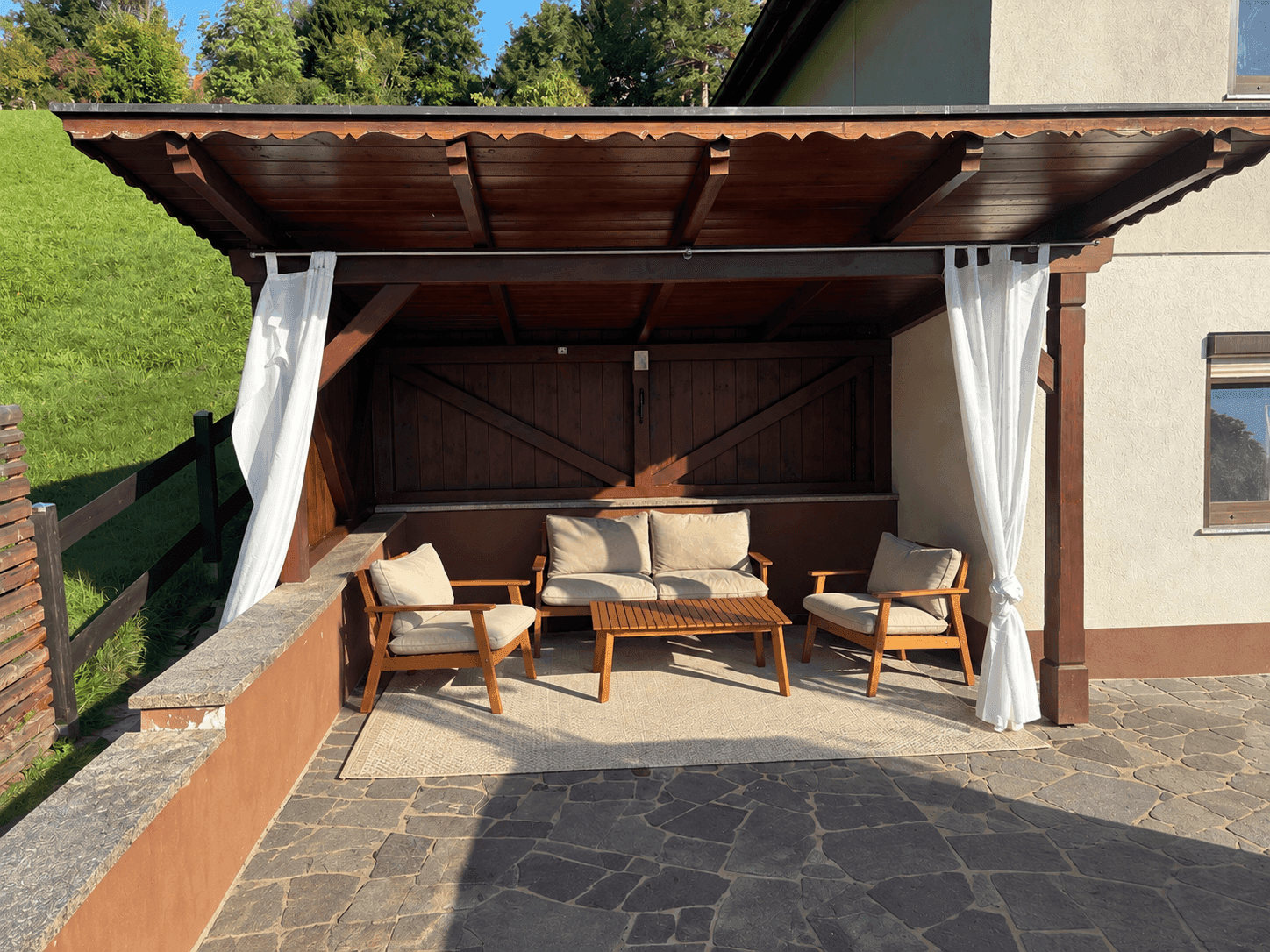 Überdachter Sitzbereich im Freien mit Holzmöbeln und Steinboden.