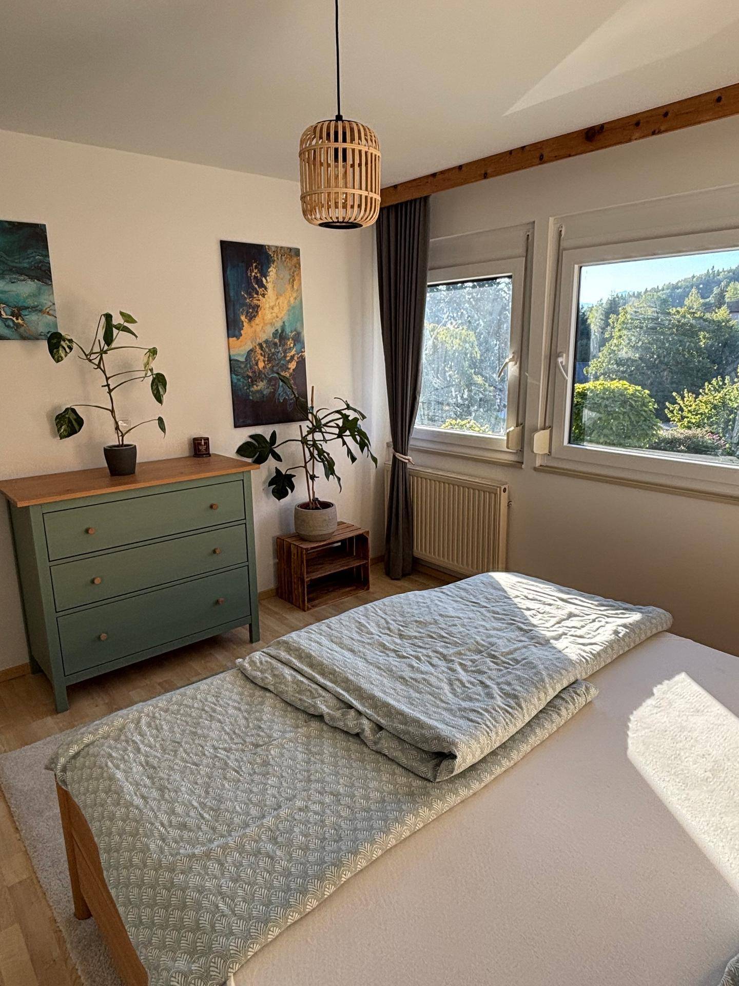 Gemütliches Schlafzimmer mit Holzbett, grüner Kommode und Blick auf die Natur.