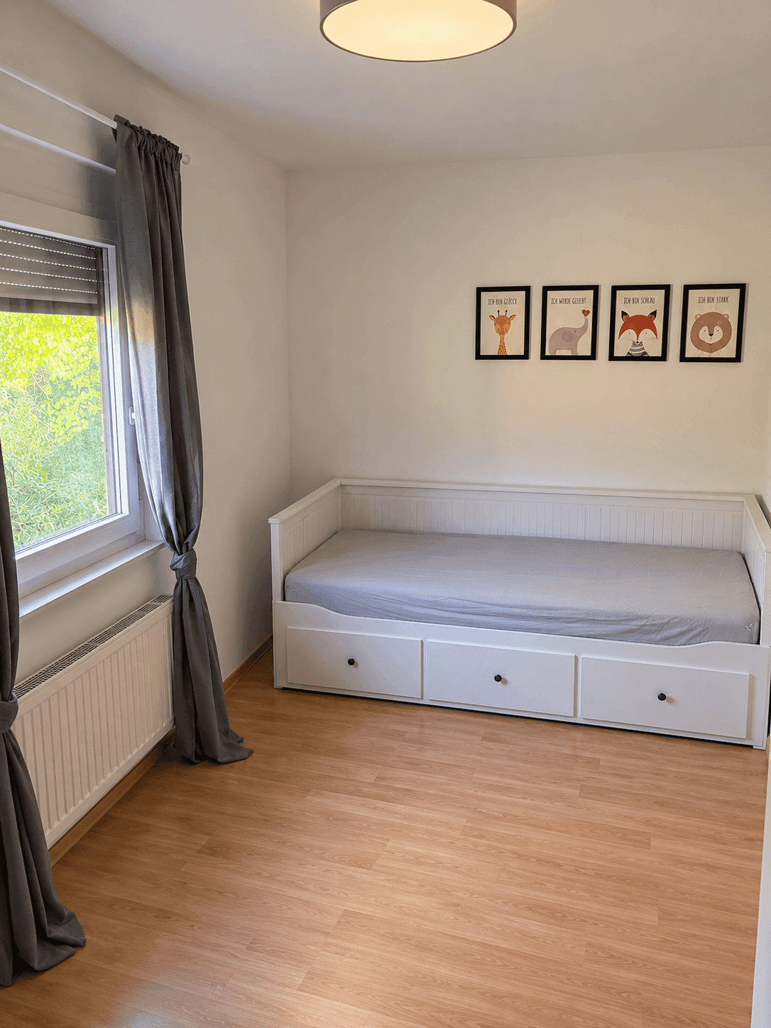 Kinderzimmer mit Tagesbett, Laminatboden und Fenster mit Blick ins Grüne.