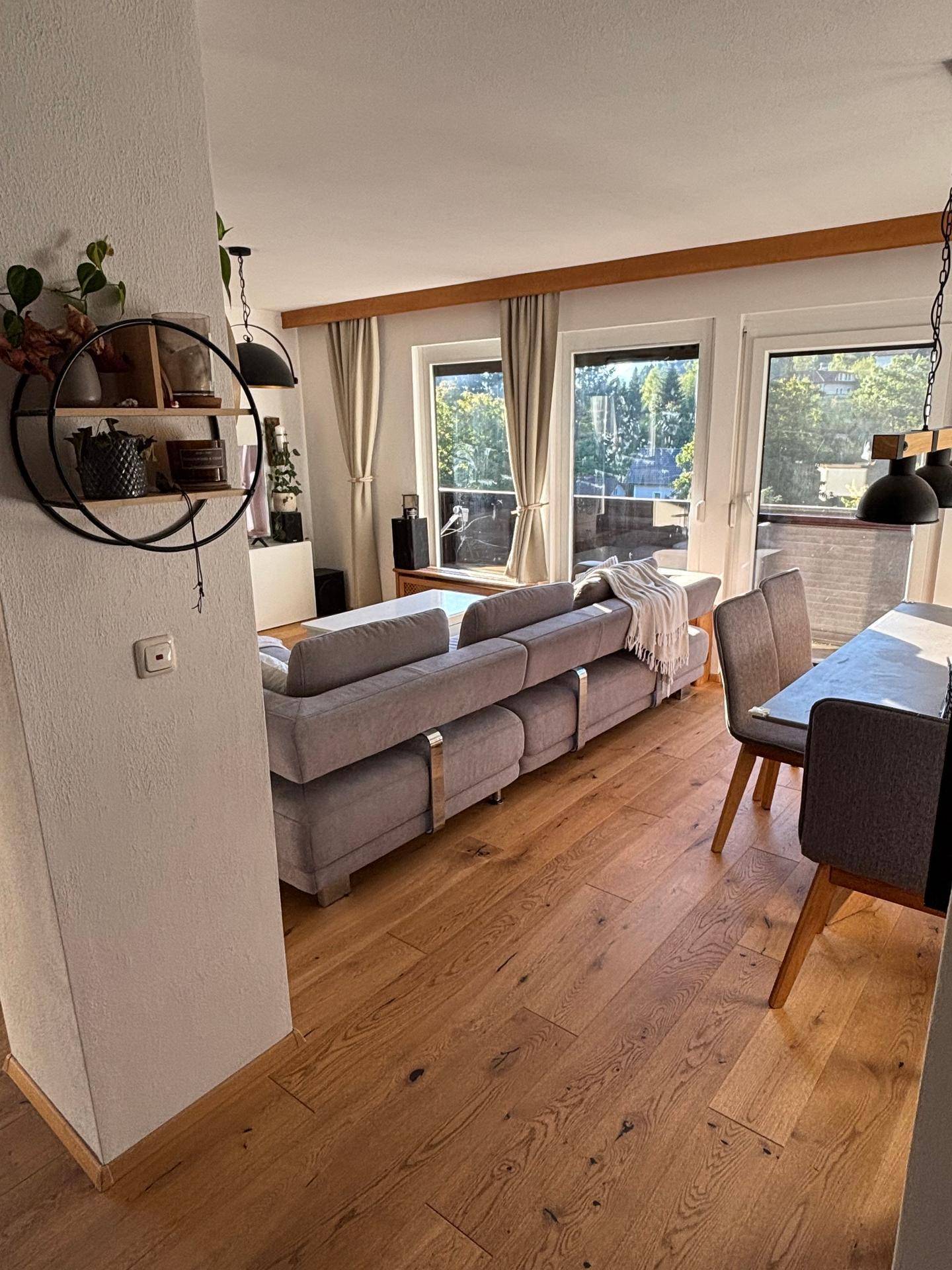 Geräumiger Wohn- und Essbereich mit Holzboden und großen Fenstern.