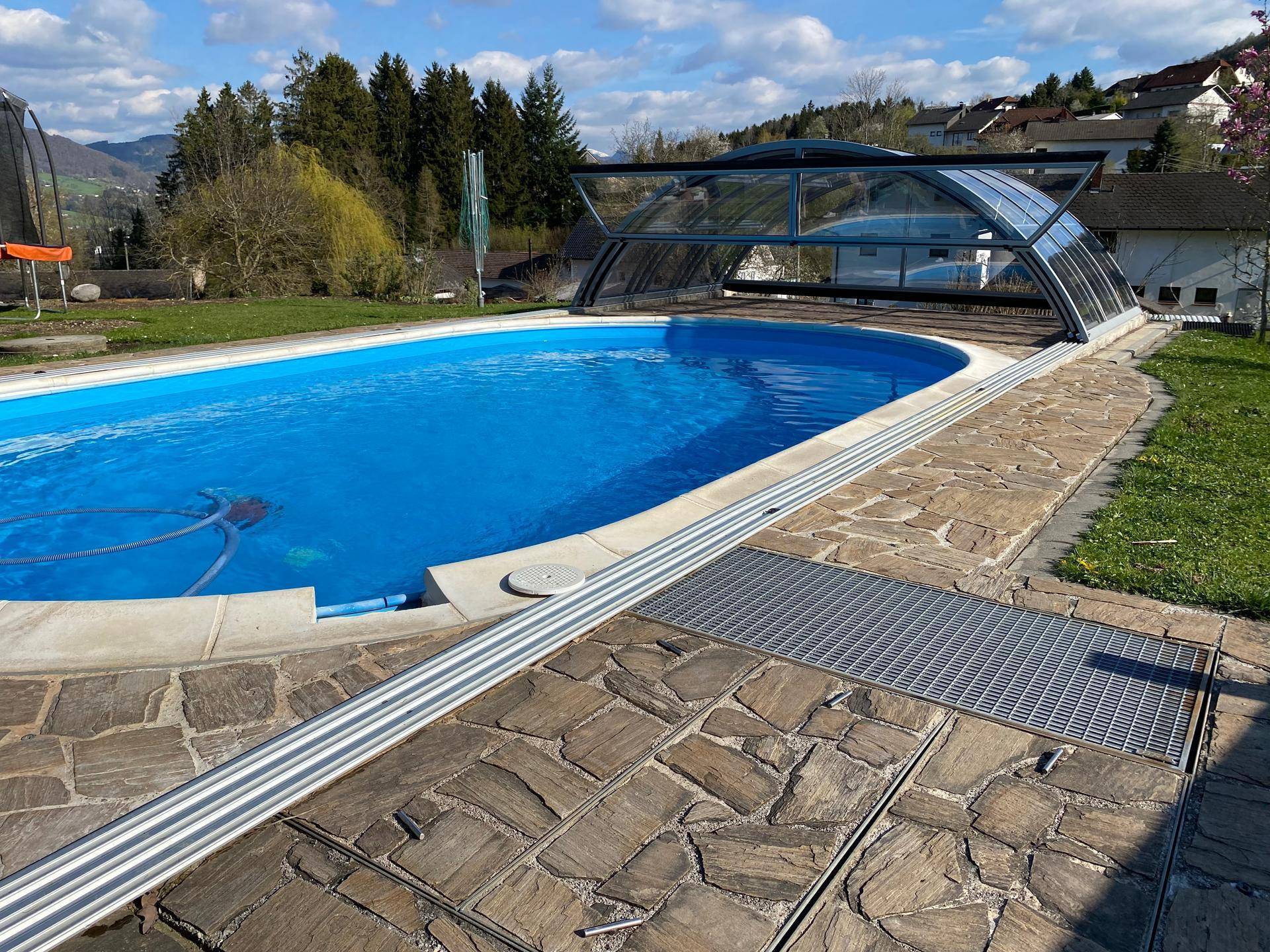 Großer Außenpool mit Überdachung und gepflasterter Terrasse im Garten.
