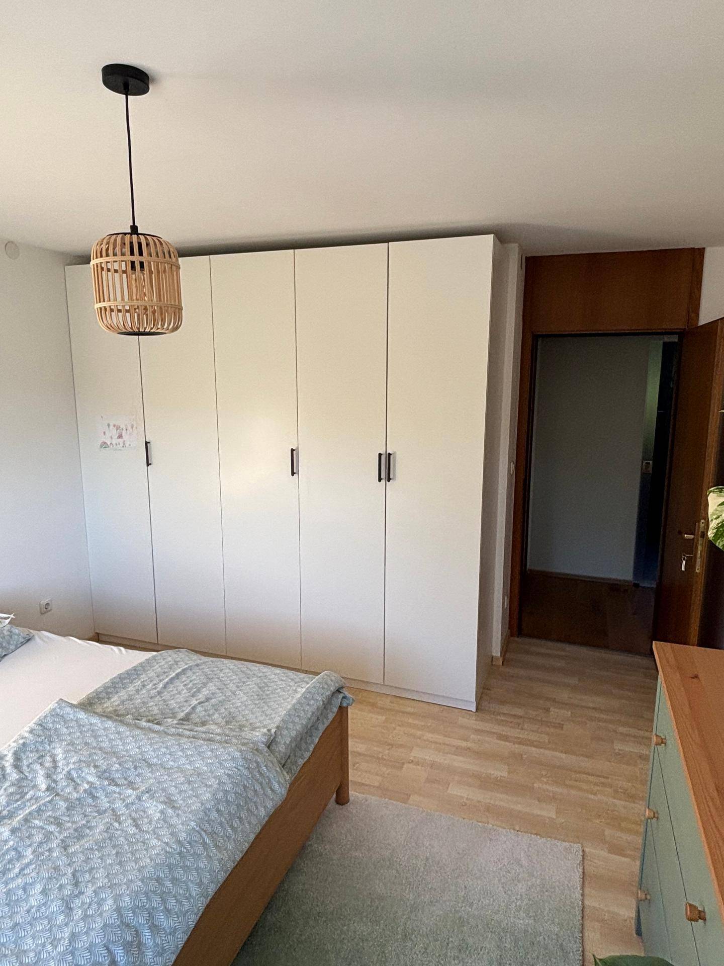 Schlafzimmer mit großem Kleiderschrank, Holzbett und hellem Laminatboden.