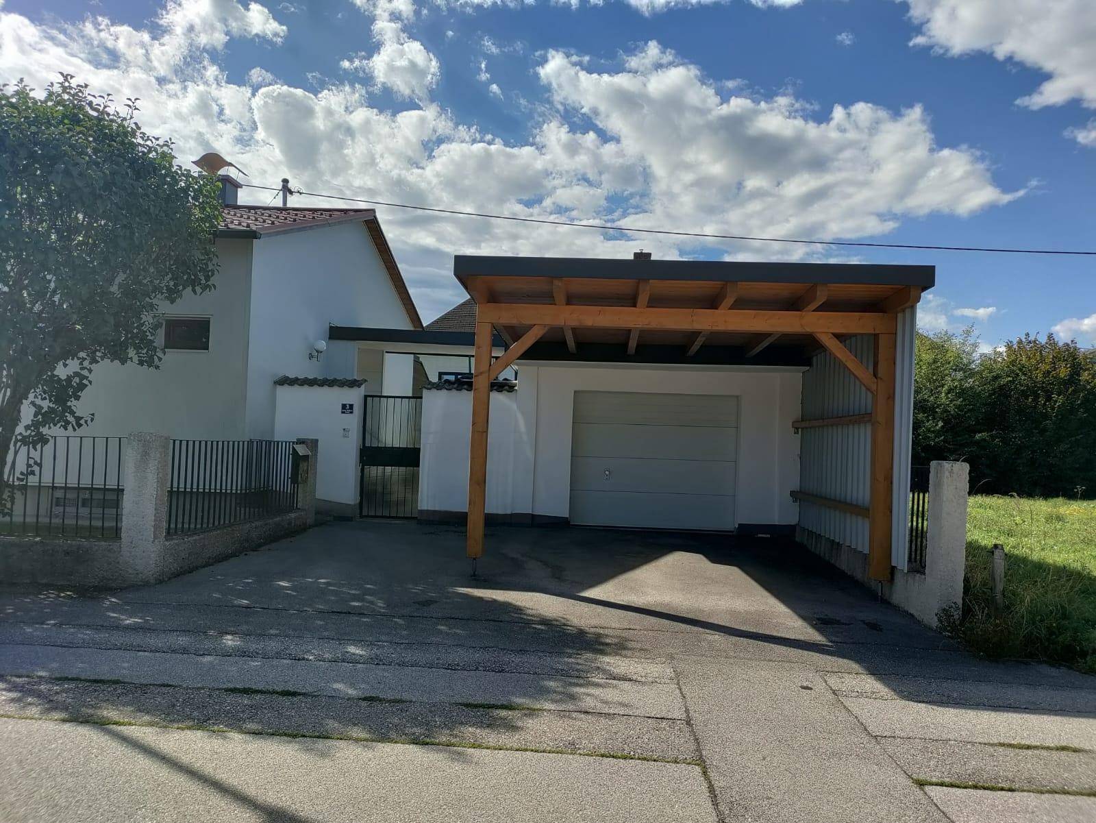 Vorderansicht des Hauses mit Einfahrt, Carport und Garage unter einem sonnigen Himmel.
