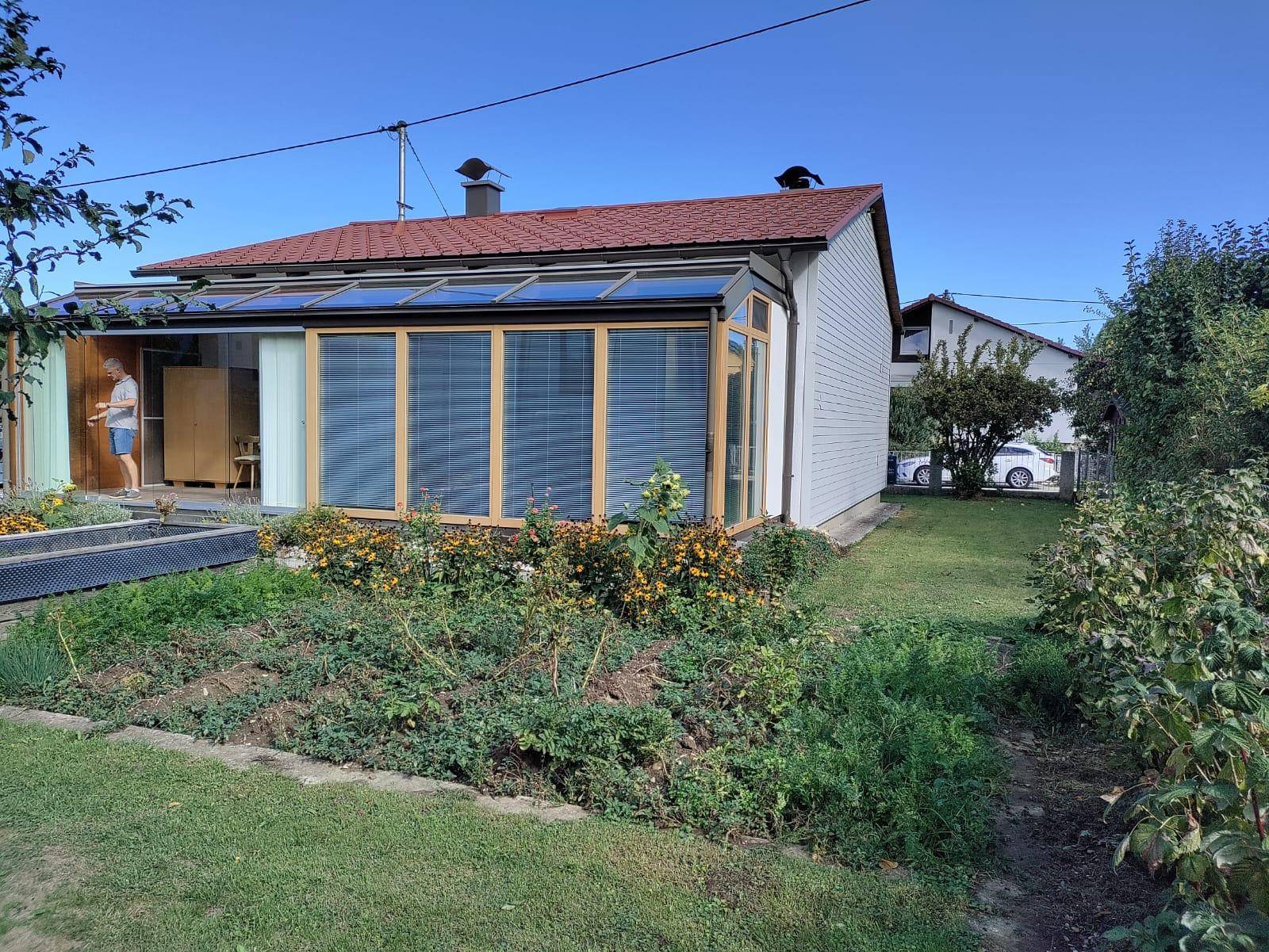 Seitenansicht des Hauses mit einem verglasten Wintergarten und angrenzendem, blühendem Garten.