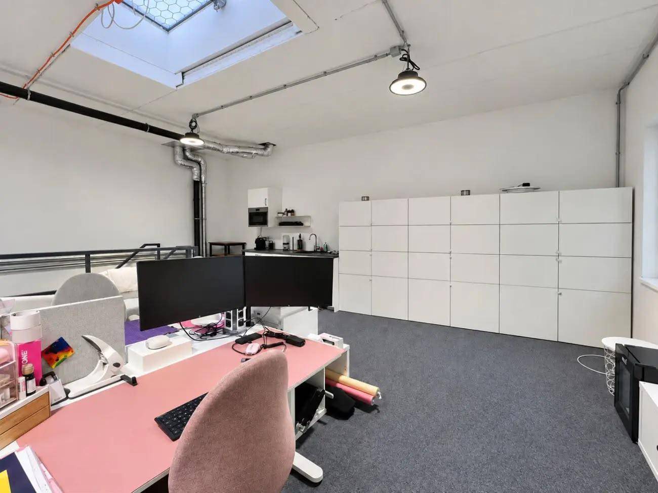 Moderner Bürobereich mit Schreibtischen, Schließfächern und einer kleinen Küchenzeile.