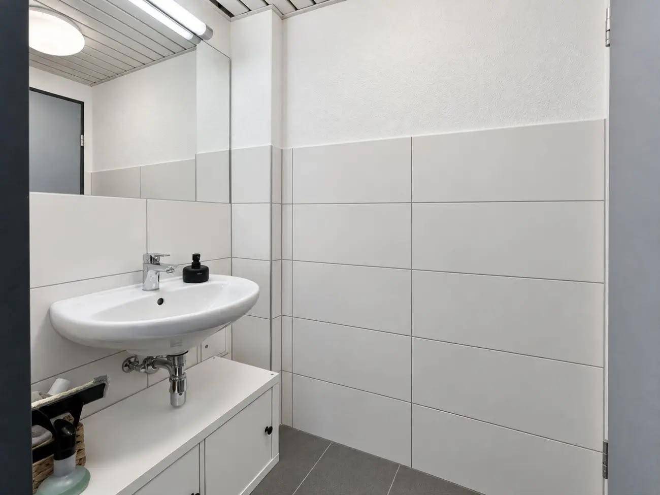 Modernes Badezimmer mit weißen Wandfliesen, einem Waschbecken und grauen Bodenfliesen.