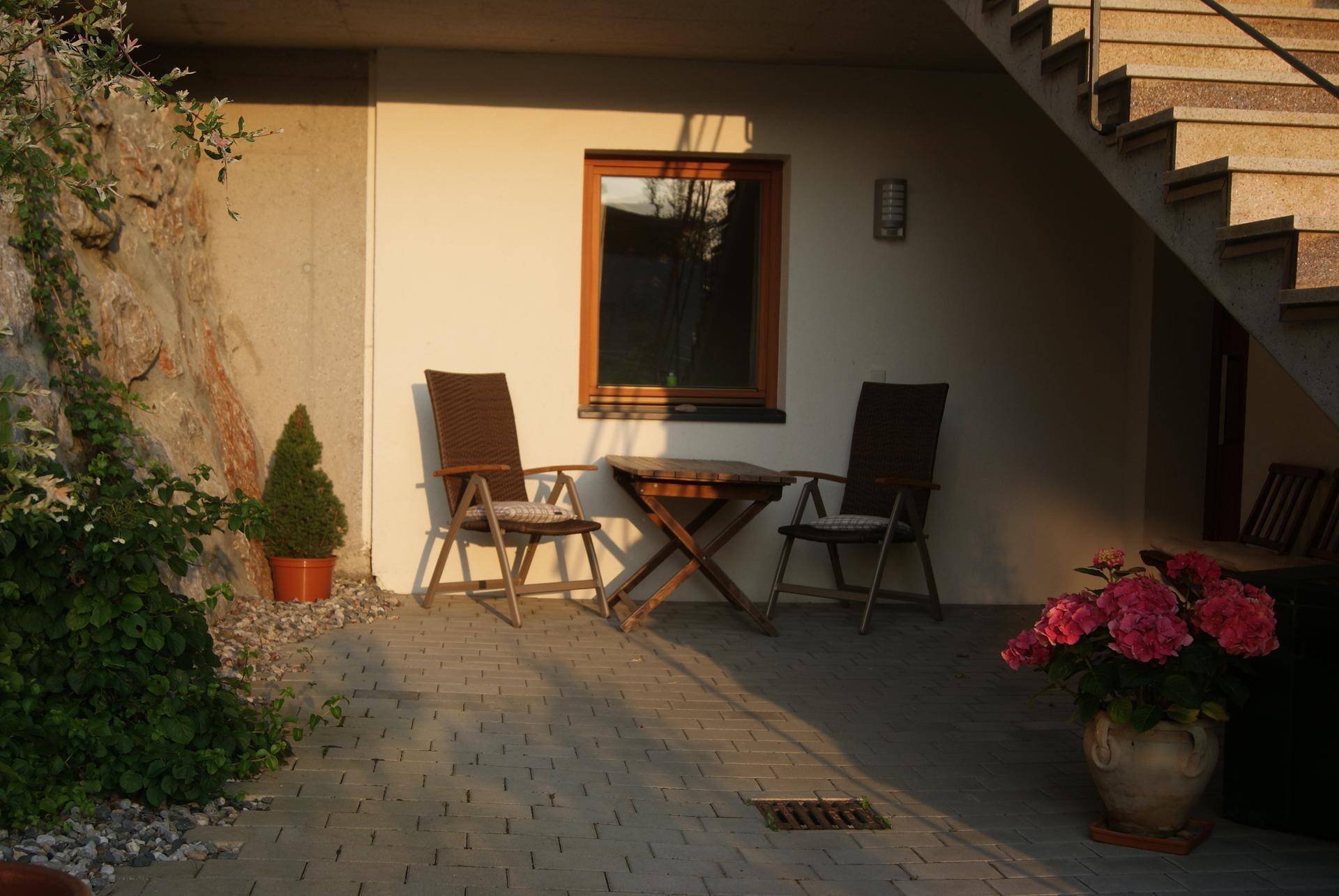 Gemütliche gepflasterte Terrasse mit Gartenmöbeln, umgeben von Pflanzen und einer Felswand, ideal für entspannte Stunden im Freien.