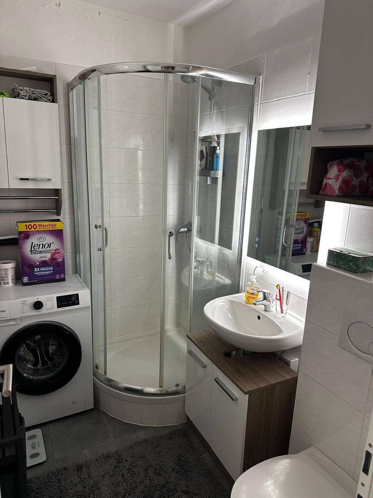 Modernes Badezimmer mit Duschkabine, Waschbecken, Toilette und integrierter Waschmaschine.