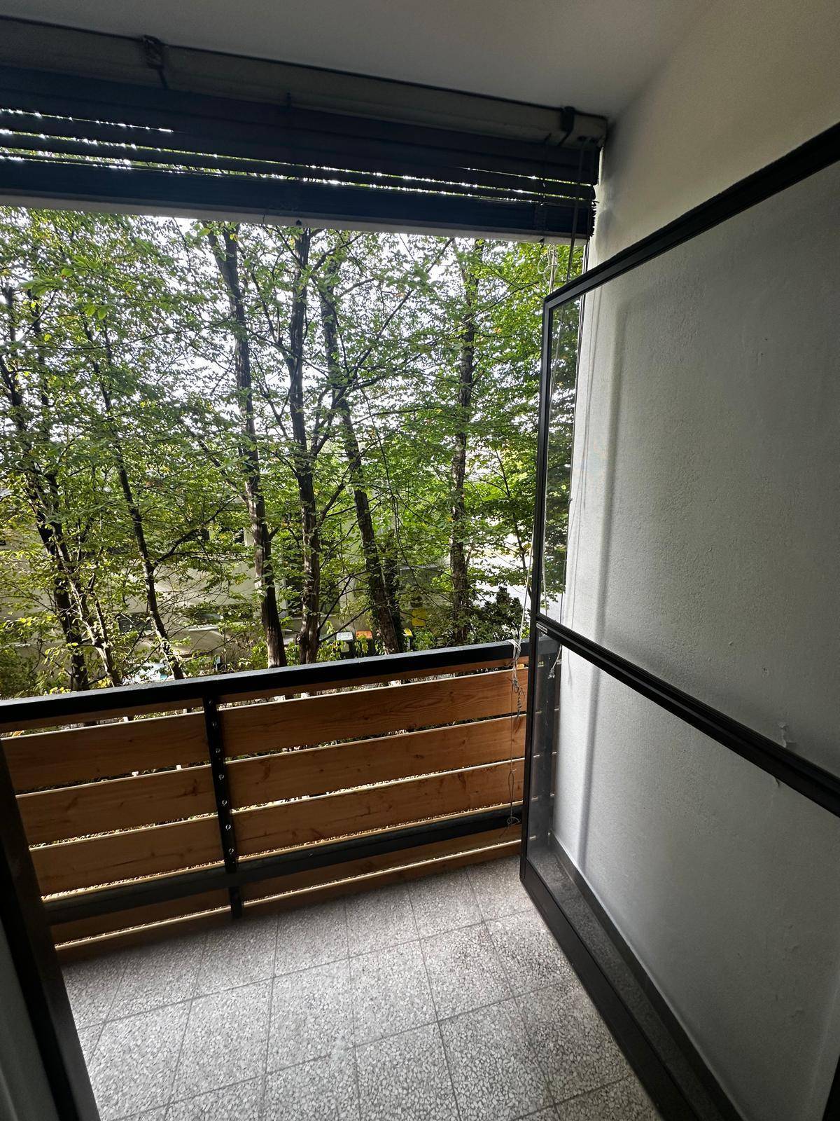 Heller Balkon mit Holzelementen und freiem Blick auf die umliegende Baumlandschaft.