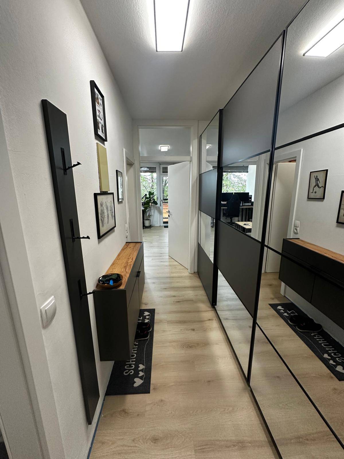 Heller Flur mit großen Spiegelschränken, schwebender Konsole und modernem Laminatboden.