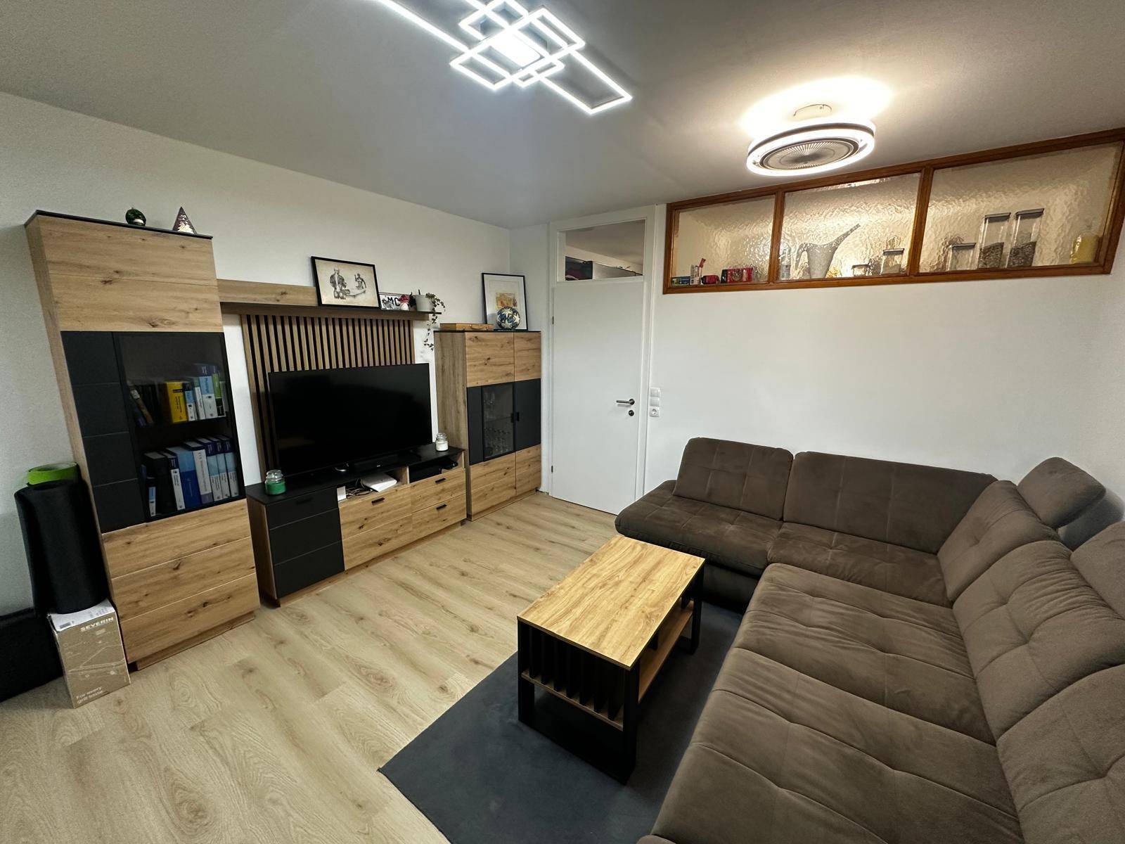 Wohnzimmer mit moderner TV-Wand, großem Sofa und dekorativer Fensteröffnung über der Tür.