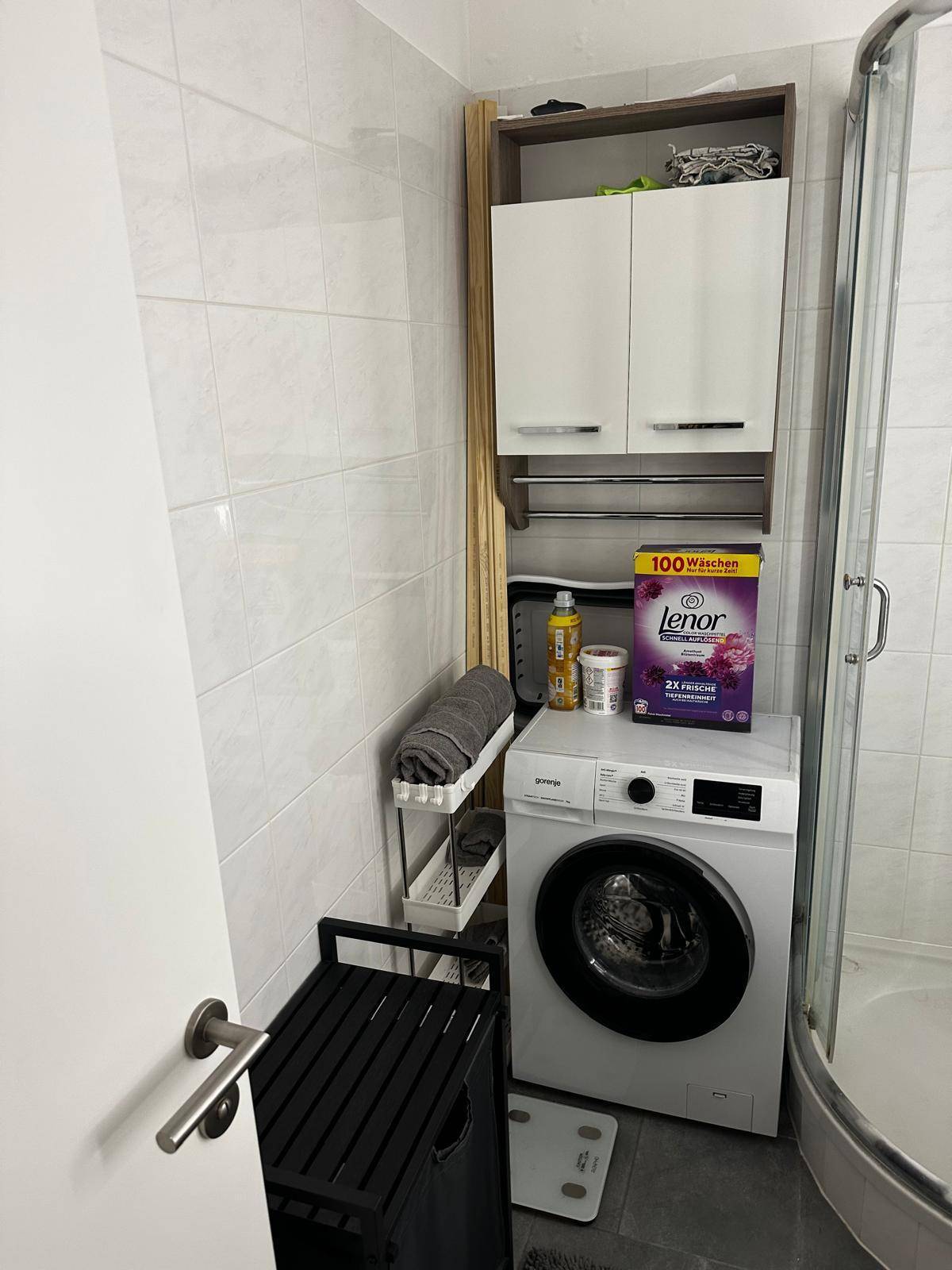 Funktionales Badezimmer mit Waschmaschine, Duschkabine und praktischen Wandregalen.