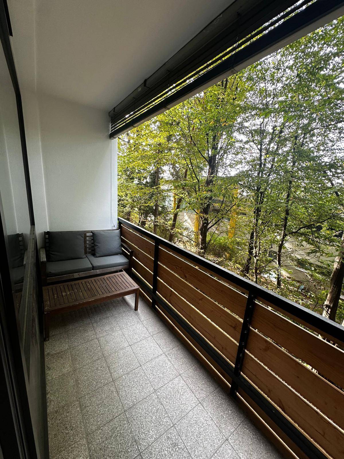 Balkon mit Holzzaun, Sitzgelegenheiten und einem schönen Ausblick auf grüne Bäume.