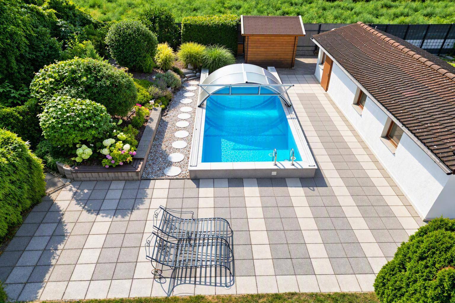 Gepflegter Gartenbereich mit Pool, großer gepflasterter Terrasse und Gartenhaus aus der Vogelperspektive.