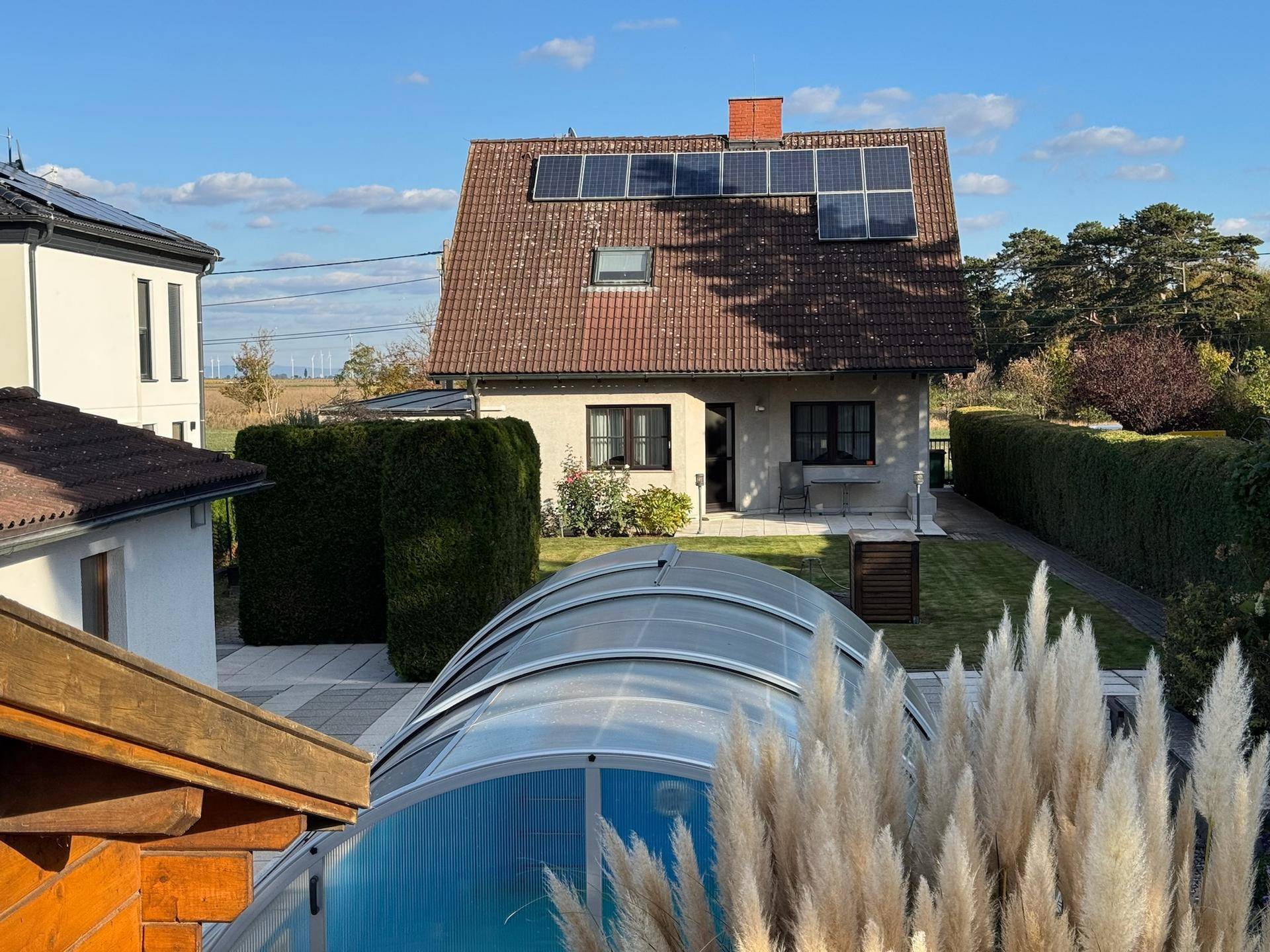 Gesamtansicht des Hauses mit Garten, Pool und Solaranlage auf dem Dach unter blauem Himmel.