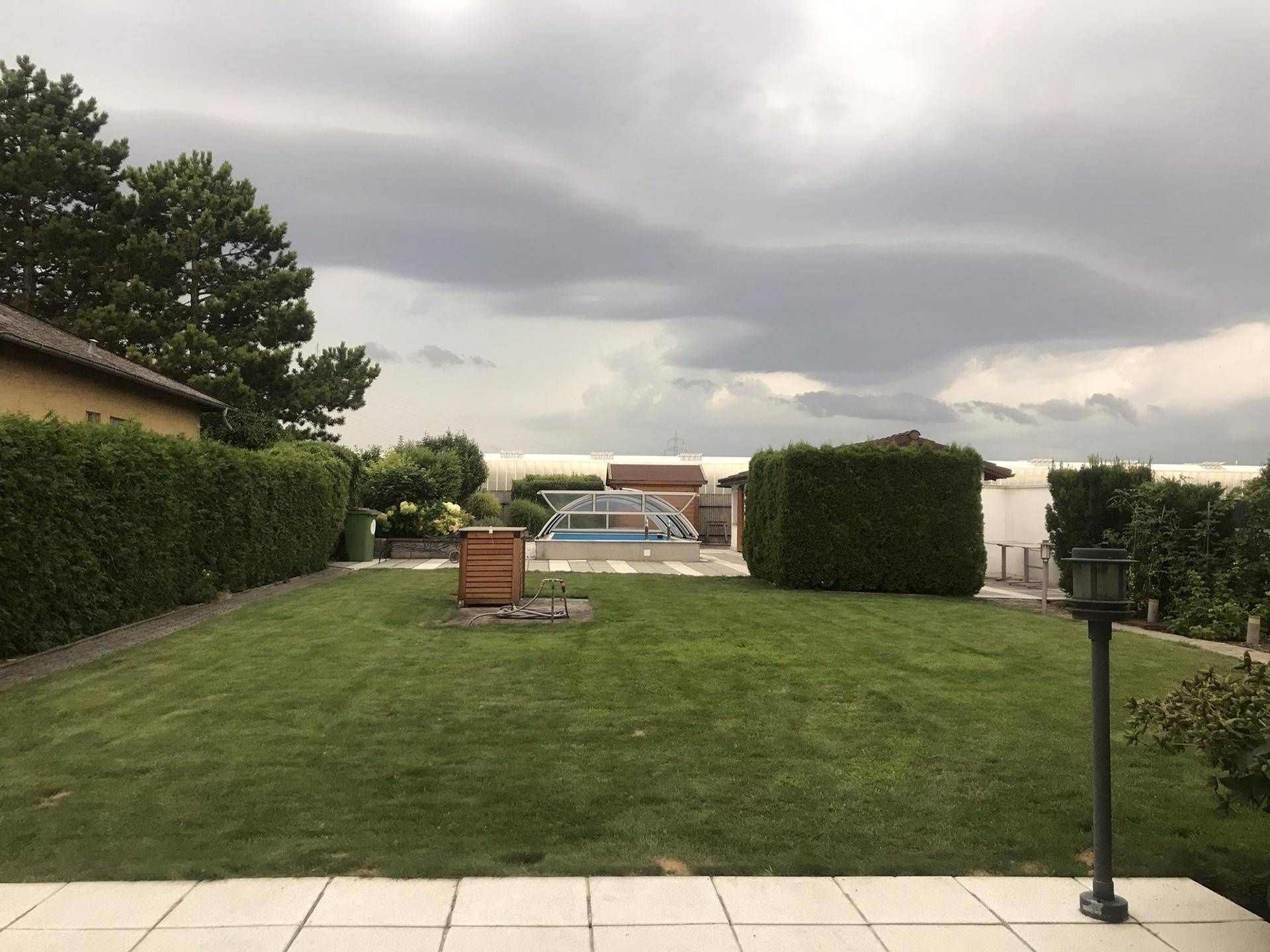 Weitläufiger Garten mit Rasenfläche, Pool und Nebengebäuden unter bewölktem Himmel.