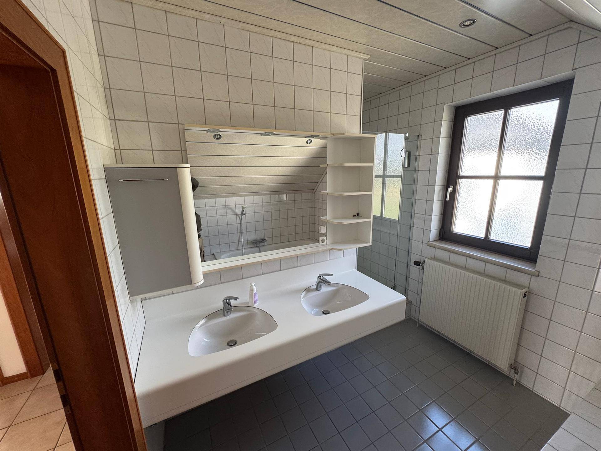 Badezimmer mit Doppelwaschbecken, Spiegelschrank und Duschbereich, hell gefliest.