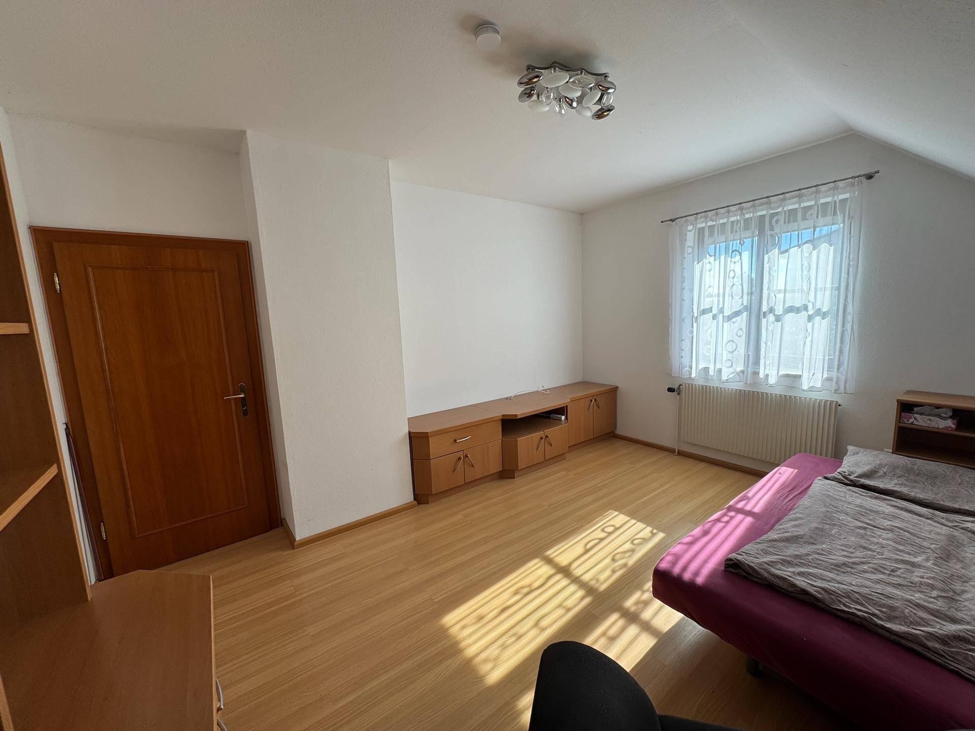 Helles Schlafzimmer mit Holzboden, Dachschräge und Fenster mit Vorhängen.