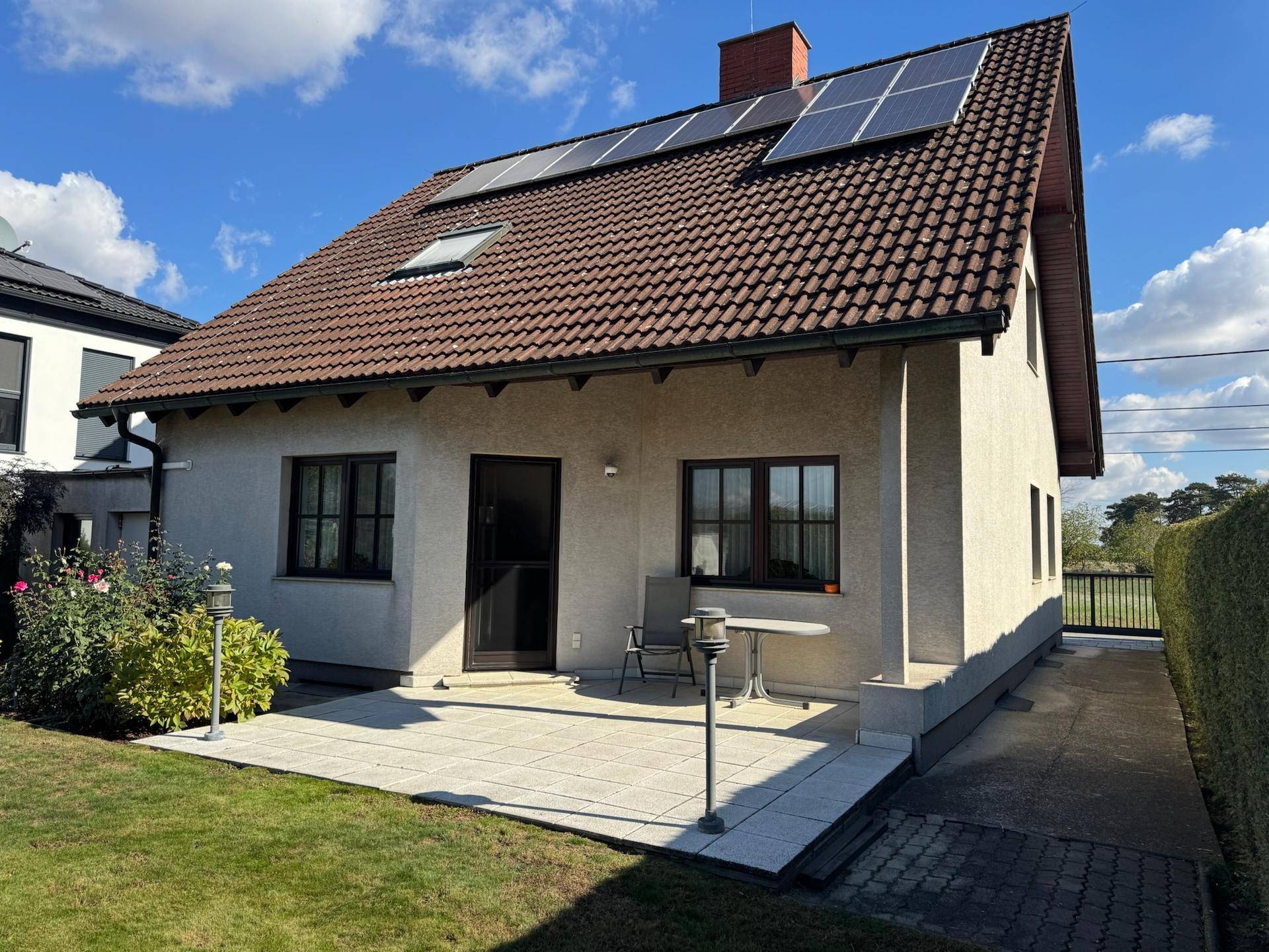 Rückseite des Hauses mit kleiner gepflasterter Terrasse, Garten und Solaranlage auf dem Dach.