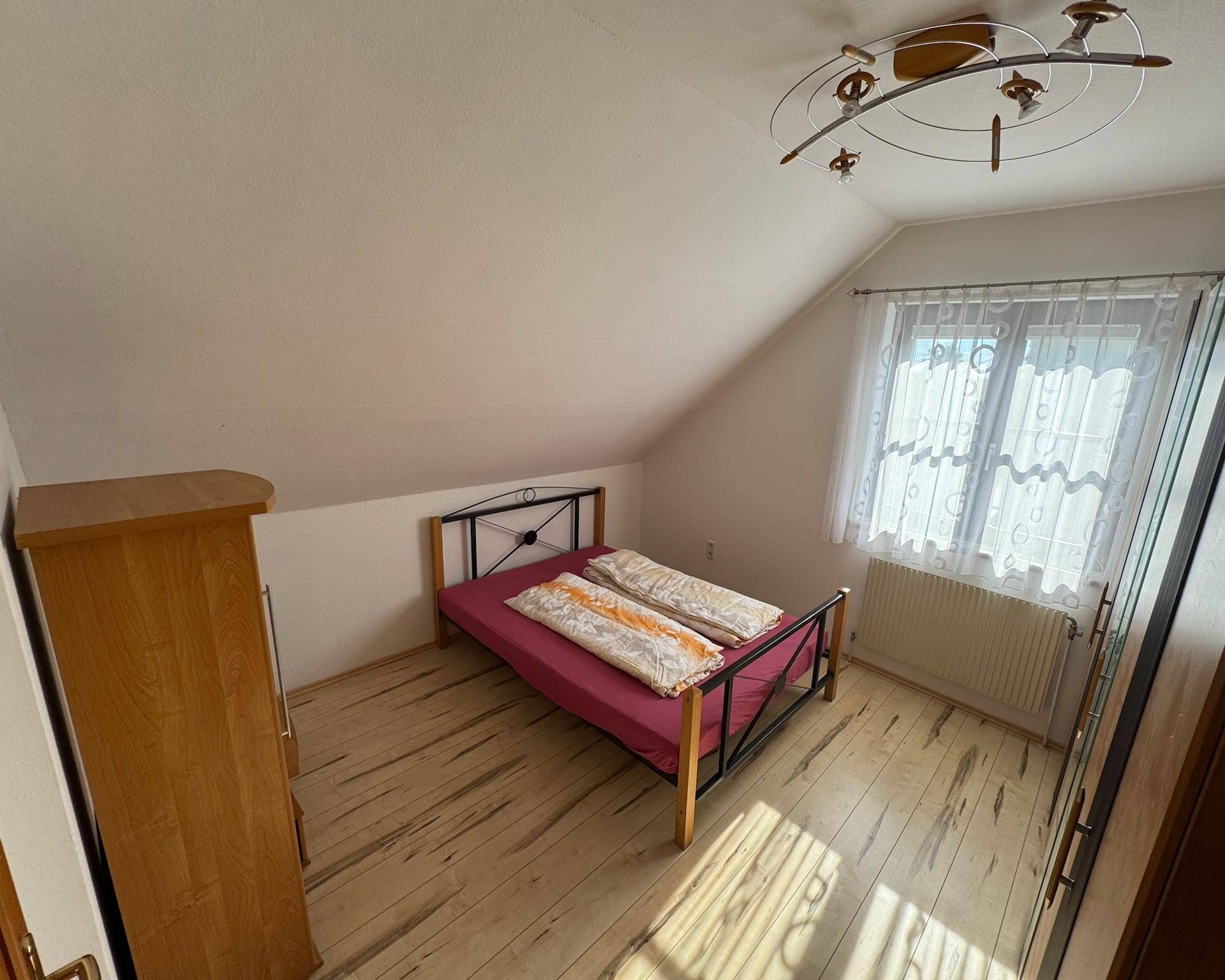 Helles Schlafzimmer mit Holzboden, Fenster und Kleiderschrank.