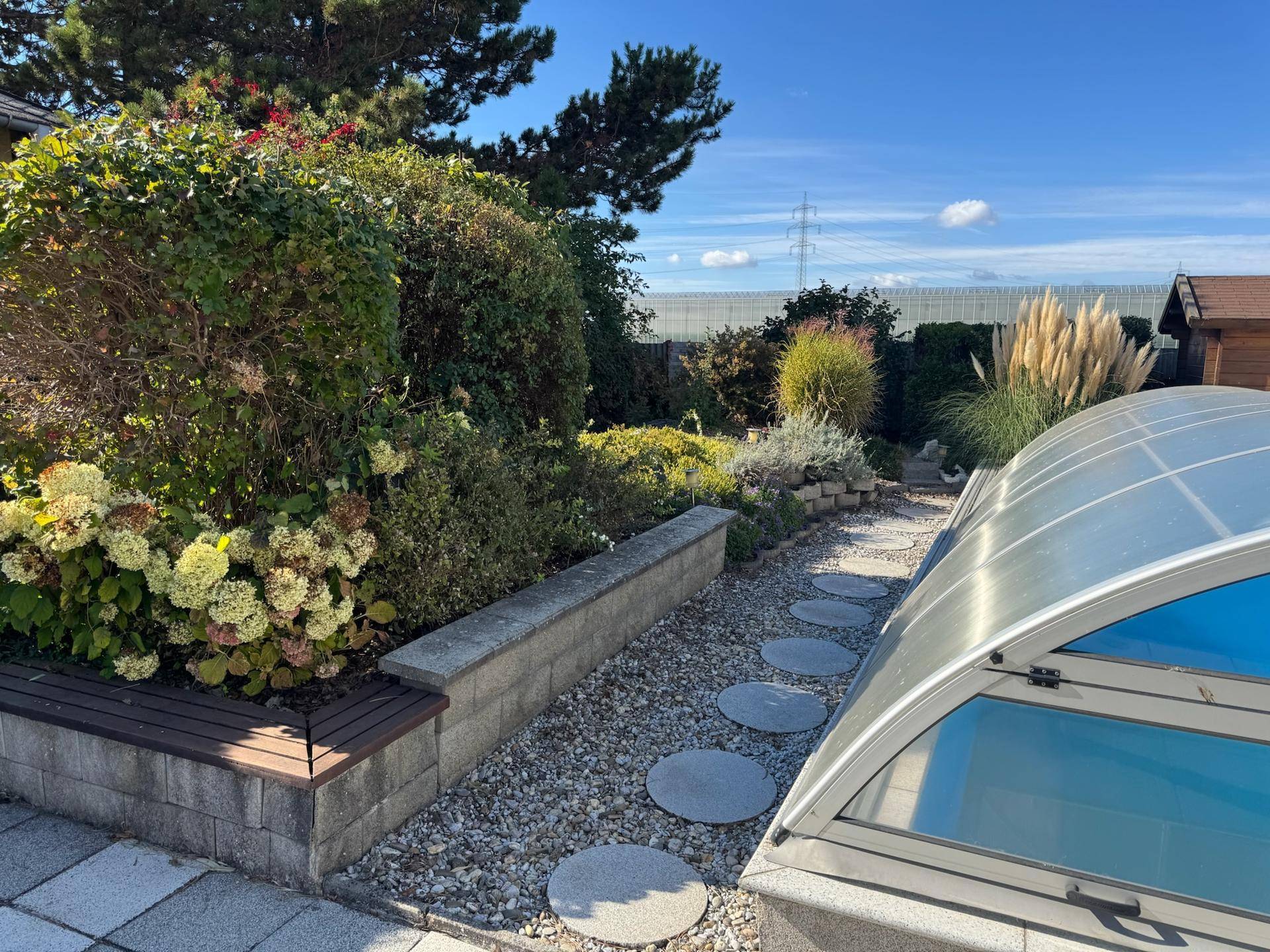 Dekorativer Gartenweg mit Trittsteinen und üppiger Bepflanzung neben dem Poolbereich.