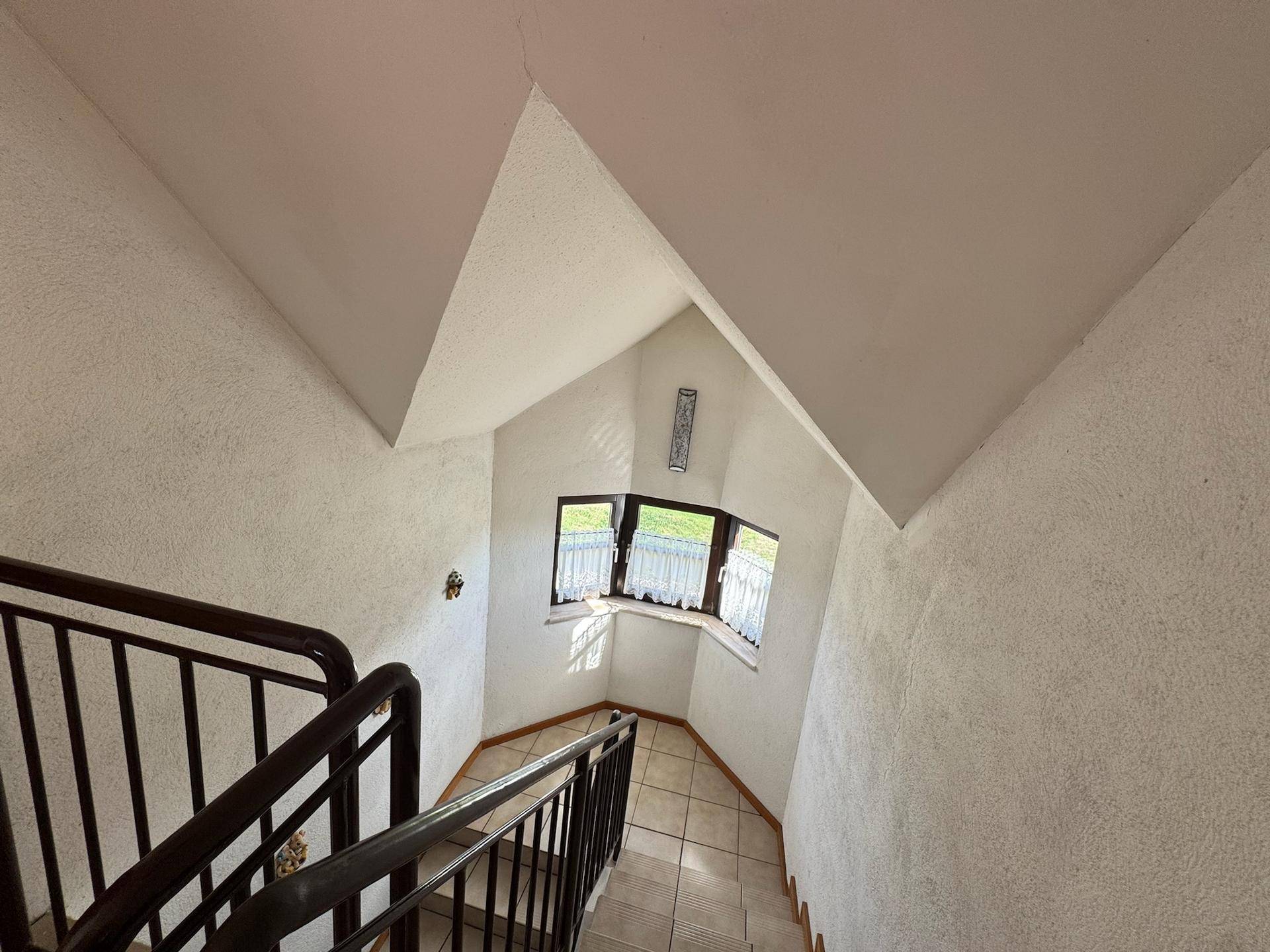 Treppenhaus mit Fliesenboden und einem Erkerfenster, das viel natürliches Licht spendet.
